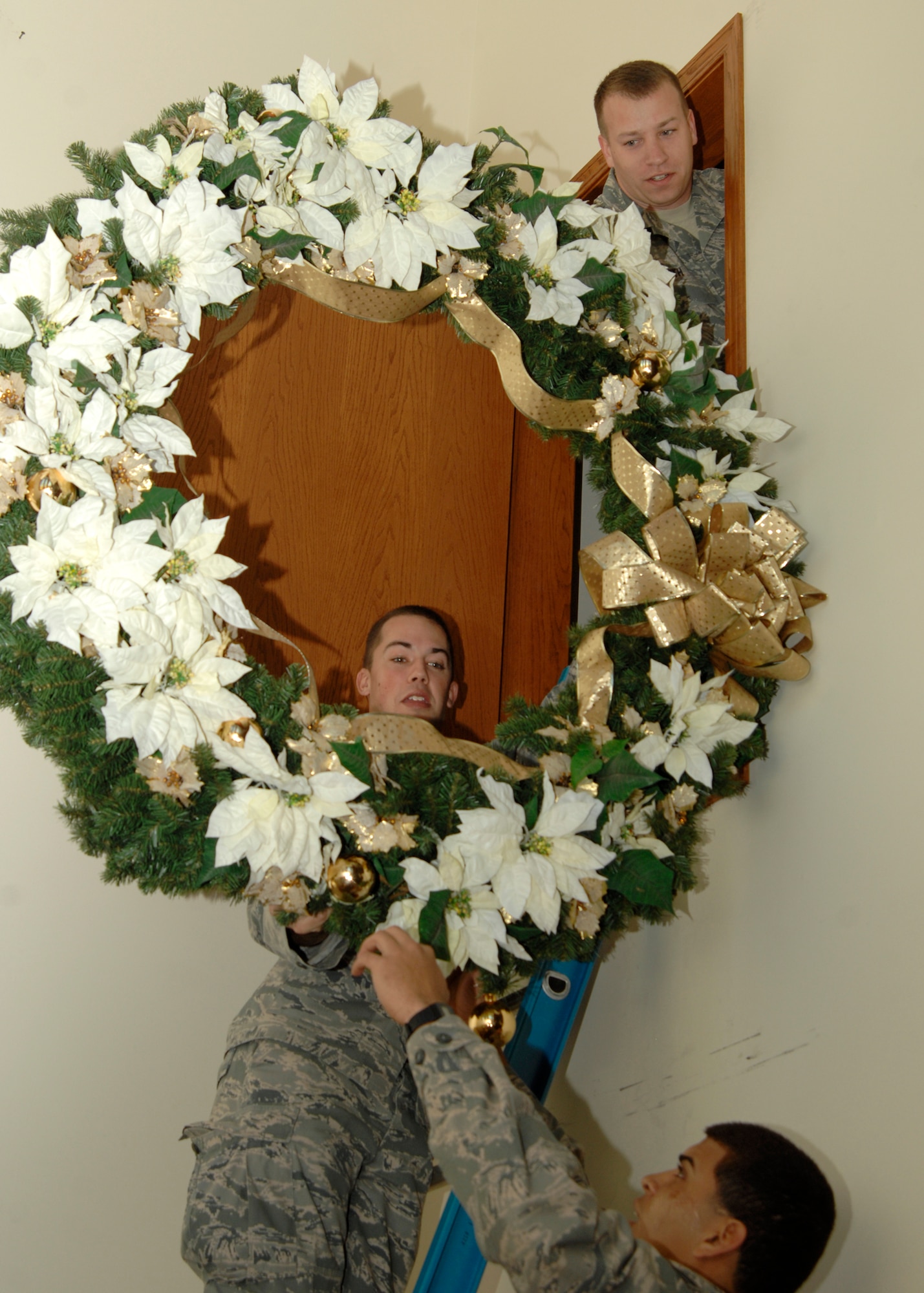 Tech. Sgt. James Smith, top, a 22nd Air Refueling Wing chaplain assistant, hands a holiday wreath to Airmen 1st Class David Dreyfus, center, 22nd Aircraft Maintenance Squadron, and Paul Rodriguez, 22nd Operation Support Squadron, Dec. 2, 2009, at the McConnell Air Force Base, Kan. Chapel. Airmen Dreyfus and Rodriguez, along with fellow First Term Airman’s Center students, helped decorate the chapel for the holidays. (U.S. Air Force Photo /Airman 1st Class Justin Shelton)