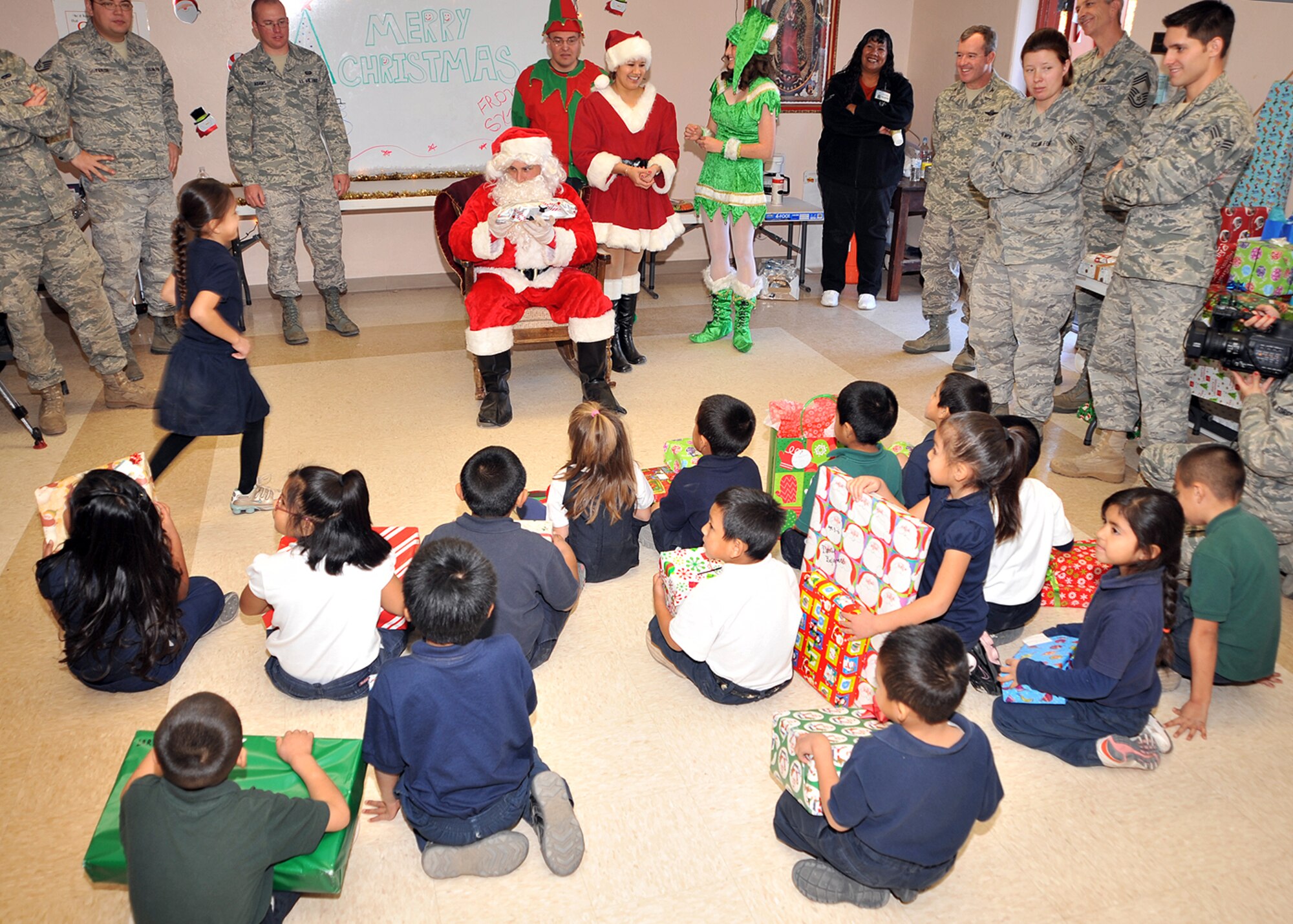 Santa and Mrs. Claus hand out presents to students from St. Xavier Mission School Dec. 17 as volunteers from D-M watch. Mr. and Mrs. Claus were at the school to host the Santas in Blue event. Airmen across D-M came together to give gifts to the children for Christmas. The St. Xavier Mission School has students from kindergarten through eighth grade. (U.S. Air Force photo/Master Sgt. Heather Cabral)
