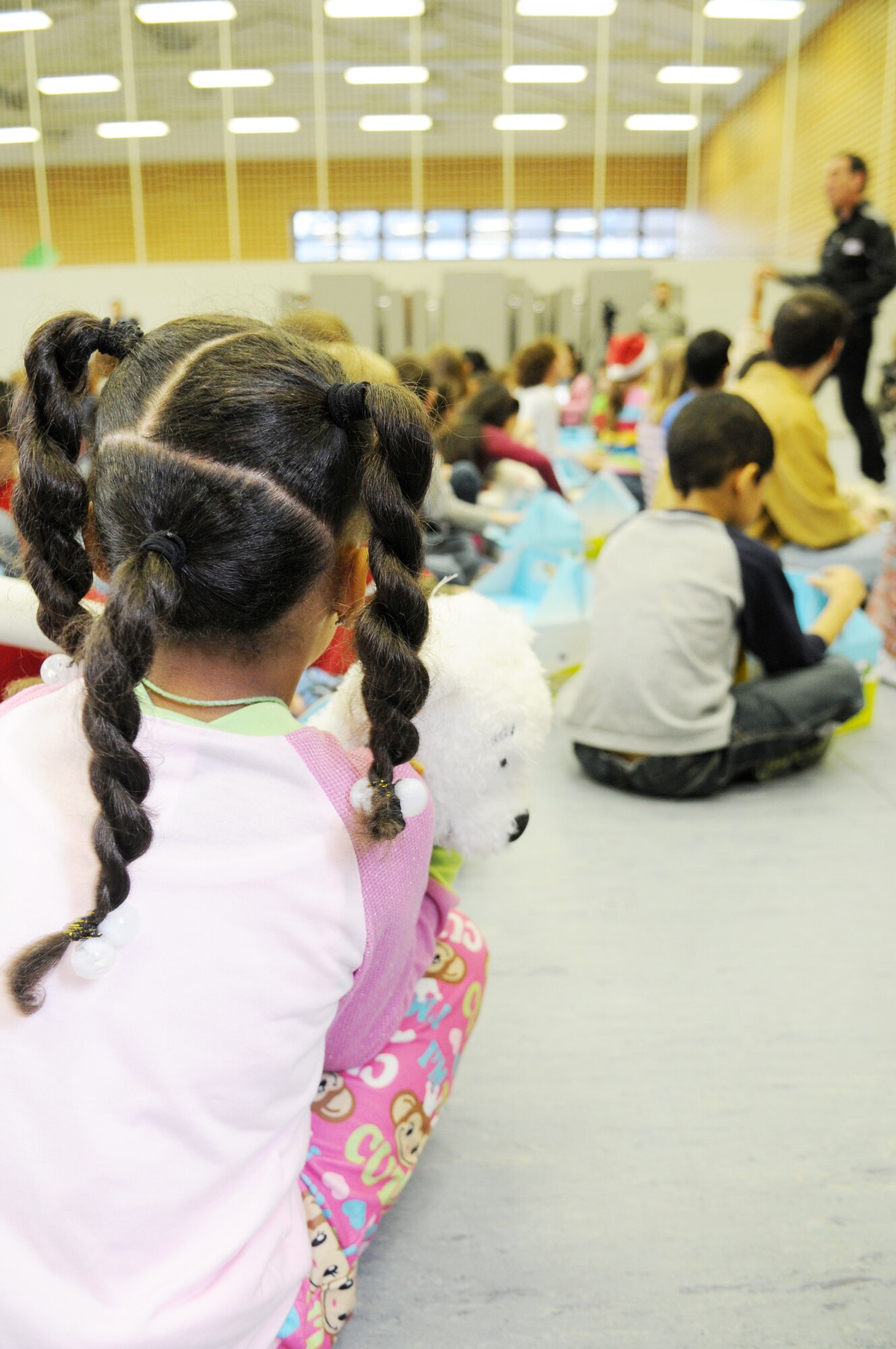 A child holds her new Cuzzie the Bear while listening to Trevor Romain at Ramstein Elementary School Dec. 17, 2009, at Ramstein Air Base, Germany. Cuzzie, who was once just a drawing in Mr. Romain's journal, is now the centerpiece of a new kit designed to comfort school-age children while their parents are deployed. Mr. Romain is a children's author. (U.S. Air Force photo/Airman 1st Class Brittany Perry)