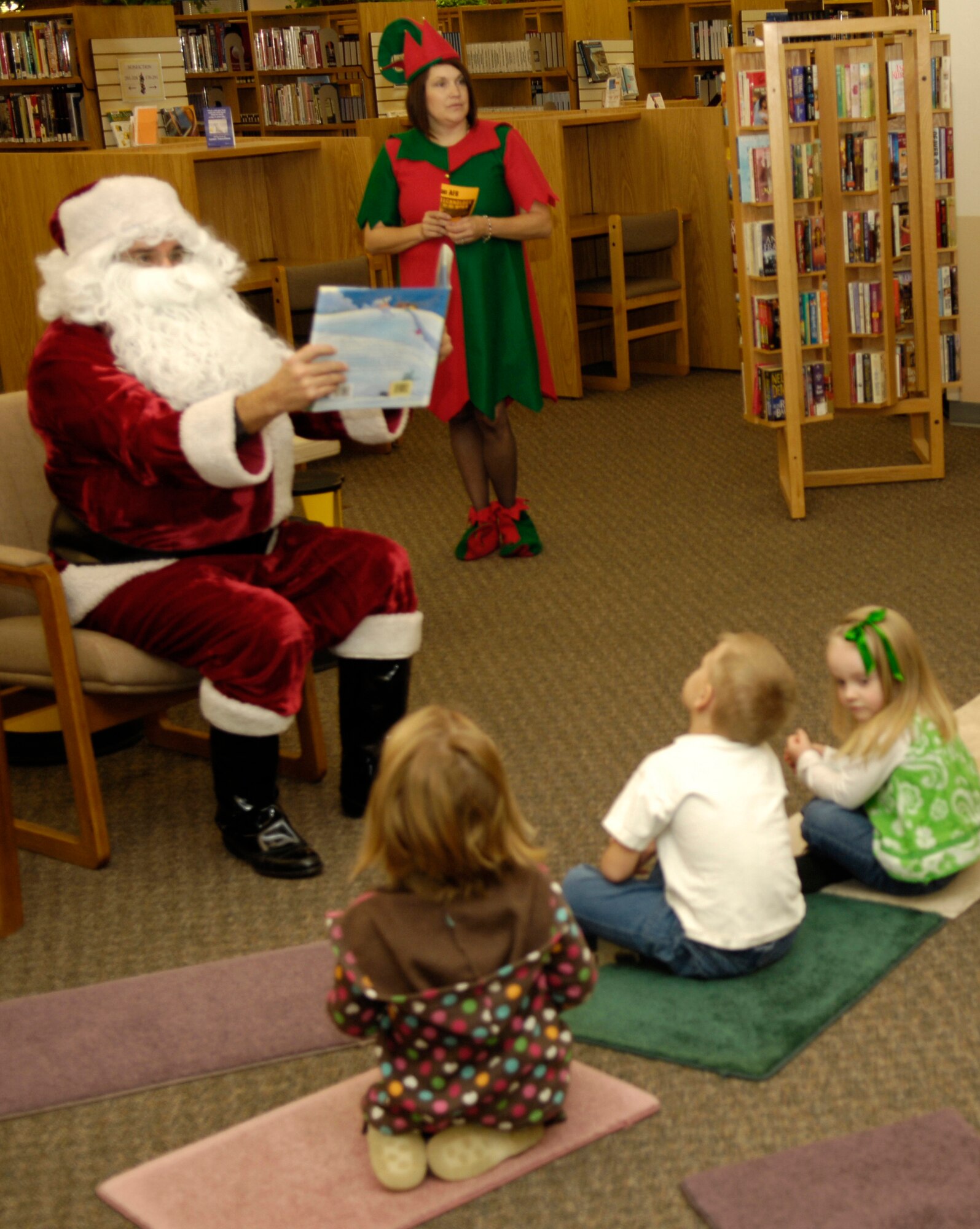 HOLLOMAN AIR FORCE BASE, N.M. -- Santa reads from a children's book while Georgia Porter, 4, Spencer Atwood, 5, and Ella Robinson, 4, listen patiently at Ahren's Memorial Library, Dec. 16. Georgia is the daughter of Maj. Maynard Porter, 846th Test Squadron, Spencer is the son of 1st Lt. Matthew Atwood, 49th Medical Group, and Ella is the daughter of  Capt. Brett Robinson, 49th Fighter Wing Legal Office. Santa made an appearance at the base library to read to Holloman children and one of his elves was also there to help. More than thirty children came to the library to hear Santa read them a Christmas story. (U.S. Air Force photo by Tom Fuller)