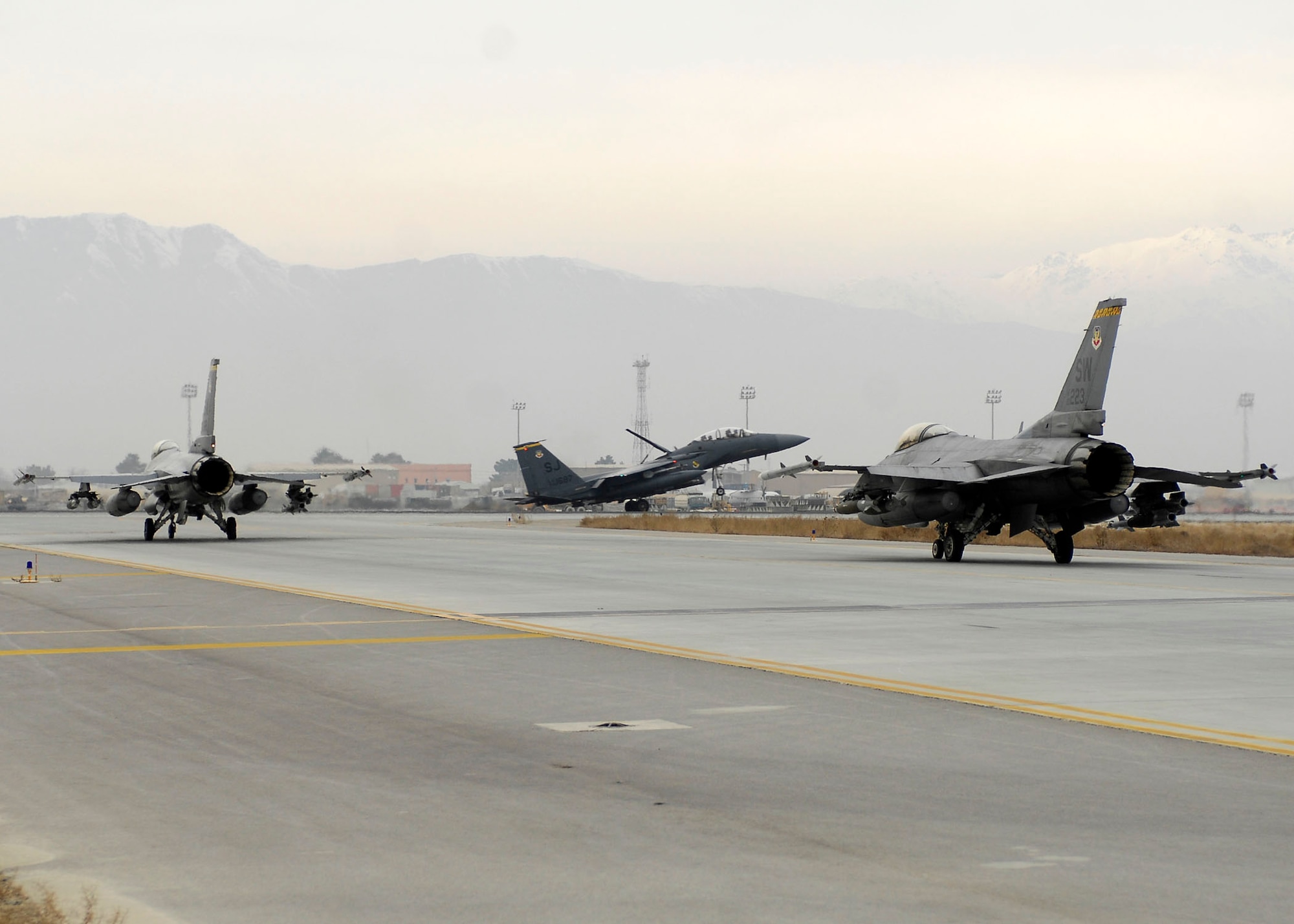 BAGRAM AIRFIELD, Afghanistan -- An F-15E Strike Eagle lands while two F-16 Fighting Falcons prepare to take off from the flightline Dec. 26, 2009. The F-15E is a dual-role fighter designed to perform air-to-air and air-to-ground missions.  The F-16 provides a relatively low-cost, high-performance weapon system for the United States and allied nations.  (U.S. Air Force photo/Senior Airman Felicia Juenke)