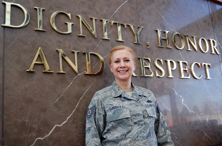 Tech. Sgt. Judy Sandoval poses in front of the Air Force Mortuary Affairs Operations Center sign stating Dignity, Honor and Respect. Sergeant Sandoval is deployed to AFMAO from Beale Air Force Base, Calif. (U.S. Air Force photo by Ed Drohan, AFMAO/PA)