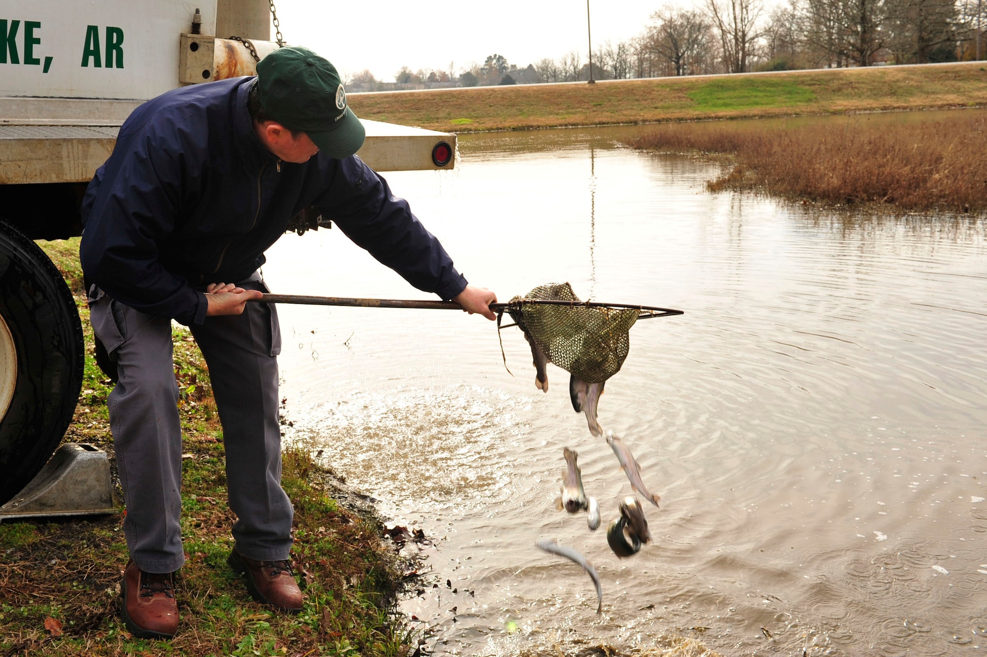 James Popham, 19th Civil Engineer Squadron natural resources manager, releases rainbow trout Dec. 16 into the small base lake. Arkansas Game and Fish Commission delivered 1,000 rainbow trout, averaging 13 inches in length and weighing 337.5 grams each. A trout stamp is required to keep a trout. (U.S. Air Force photo by Airman 1st Class Lausanne Pacheco)