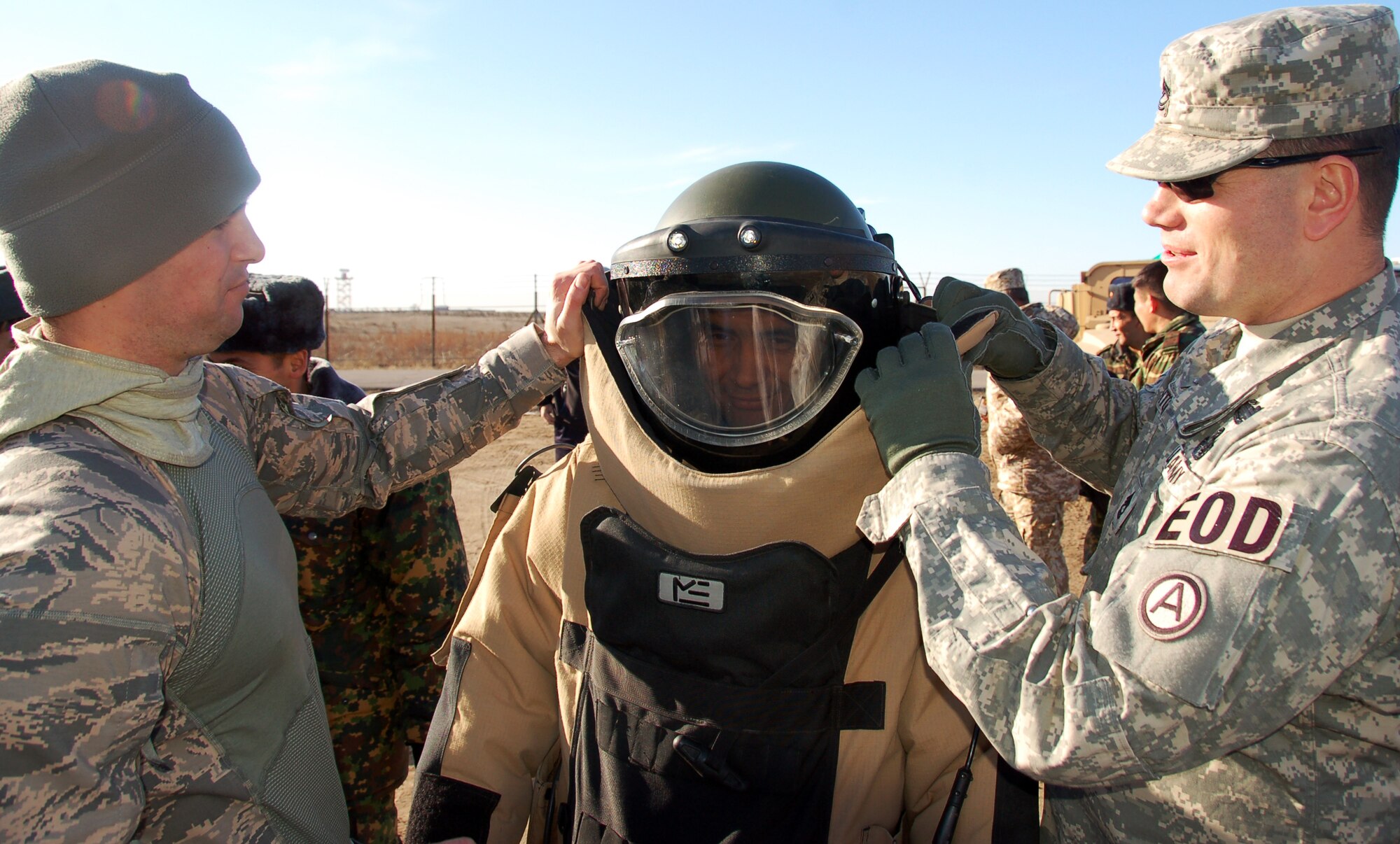 TRANSIT CENTER AT MANAS, Kyrgyzstan – Kyrgyz Lt. Col. Kadyrov Almazbek tries on an explosive ordnance disposal protection suit and helmet while (far left) Tech. Sgt. Joseph Deslauriers and Army Sgt. 1st Class Stephen Fitch help out during the Kyrgyz Ministry of Defense team’s visit to learn about EOD operations from Airmen here Dec. 15,2009.  Sergeant Desalauriers, an EOD technician here, is assigned to the 376th Expeditionary Civil Engineer Squadron. (U.S. Air Force photo/Staff Sgt. Olufemi Owolabi)