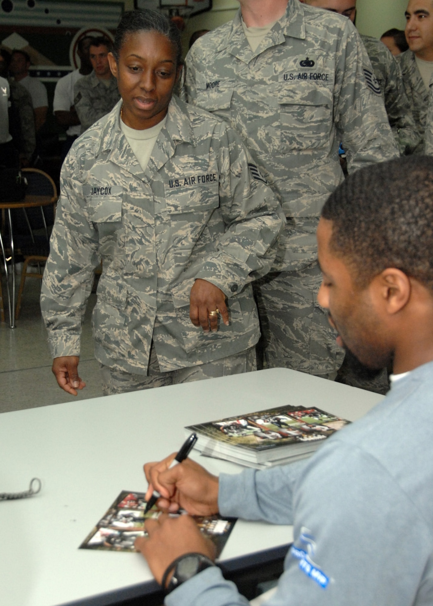 SOUTHWEST ASIA -- Staff Sgt. Clara Jaycox, 386th Expeditionary Force Support Squadron, watches as Seattle Seahawk Josh Wilson signs his autograph at an air base in Southwest Asia, Jan. 31. New England Patriot Sammy Mooris, and  Kansas City Chief Willie Roaf, and three Raiderette cheerleaders also signed autographs for the troops. (U.S. Air Force photo/Senior Airman Courtney Richardson)