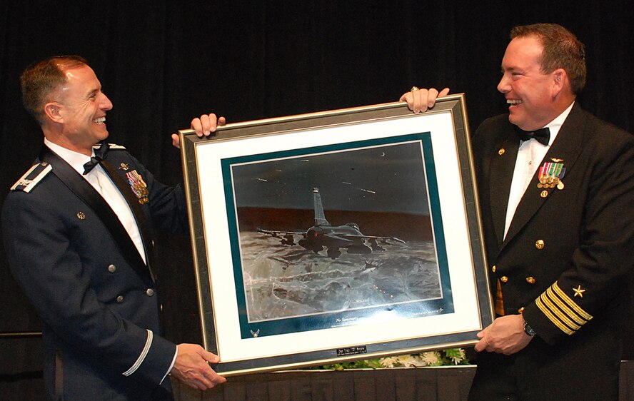 Col. Kevin Pottinger, 301st Fighter Wing commander (left) presents Navy Capt. T.D. Smyers, Naval Air Station Joint Reserve Base Fort Worth's installation commander with a lithograph titled "No Sanctuary" during the Third Annual Awards Banquet. The picture is an artist rendention of 457th Fighter Squadron's F-16Cs "Spads" bombing Afgan positions following the attacks of 9/11. Capt. Smyers was the guest speaker for this year's event at the Hilton Downtown Fort Worth. (U.S. Air Force Photo/Laura Dermarderosian-Smith)