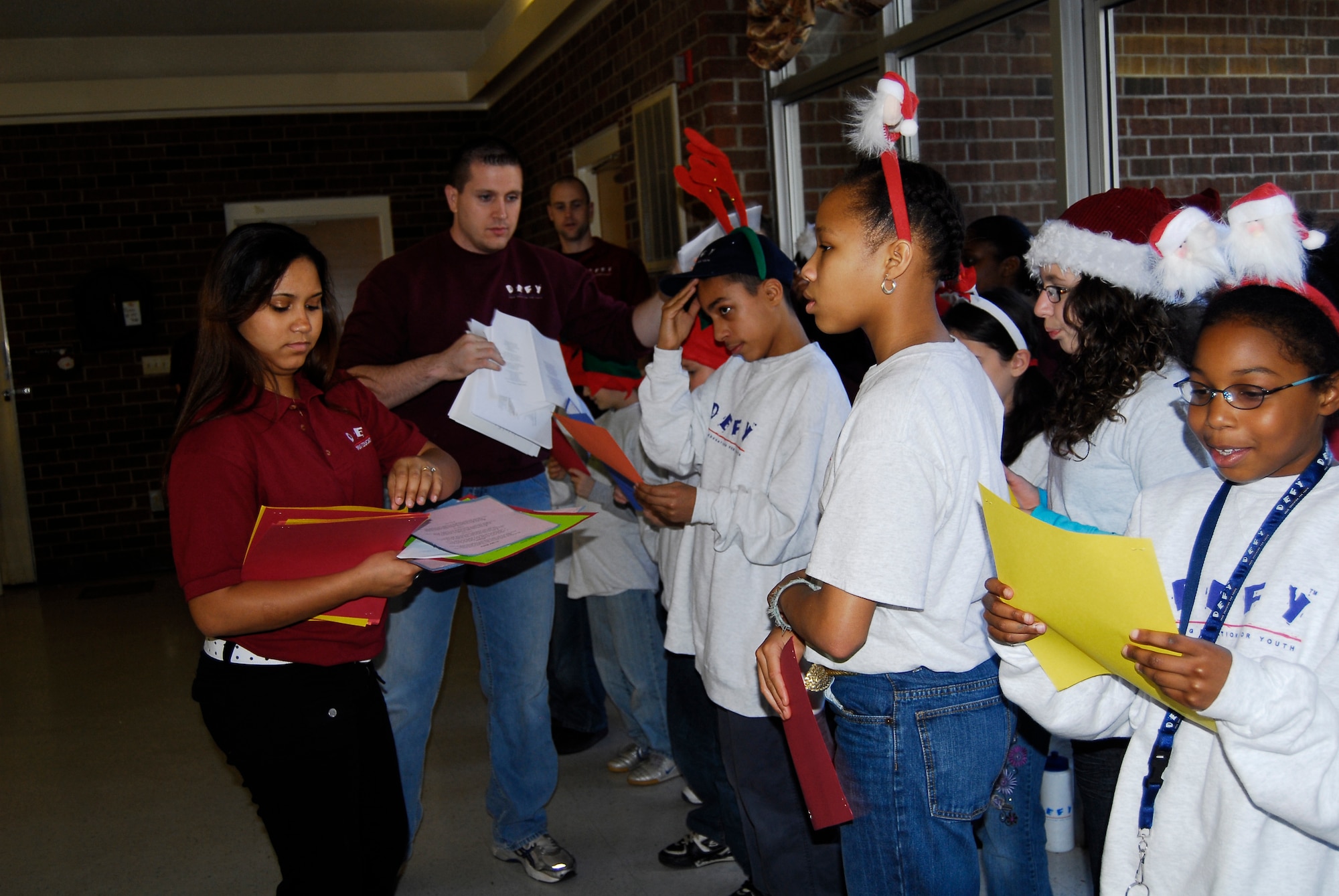 Drug Education for Youth mentors Airman 1st Class Yesenia Ramirez (left), 43rd Airlift Wing Command Post, Airman 1st Class Leroy Ford (center) and Airman 1st Class Aaron Gemalsky (back right), both from the 43rd Communications Squadron hand out song books to the DEFY children at the Highland House nursing home in Fayetteville Dec. 13. DEFY is a program for Pope youth to attend once a month and for two weeks out of the summer and educates them on drugs. Each volunteers are needed from Pope organizations to be mentors to the DEFY children. (U.S. Air Force Photo by Airman 1st Class Mindy Bloem)