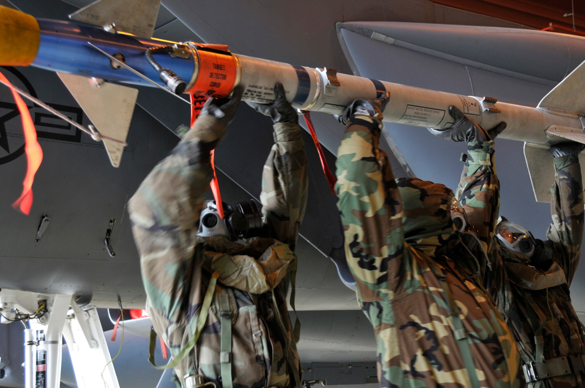 Staff Sgt. Tony Phillips, Tech. Sgt. Robert Rutland and Airman 1st Class Eric McCain, 48th Aircraft Maintenance Squadron weapons load crew members, lift an AIM-9 Sidewinder onto the launcher Jan. 27 at RAF Lakenheath, England. The load crew was being qualified on loading munitions in MOPP 4 for their crews certification training. (U.S. Air Force photo by Airman 1st Class Perry Aston) 