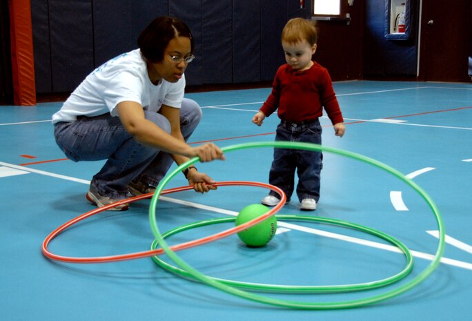 Lyvonnia Hyche shows Vincent Bustillo how to trap the ball with hula-hoops in the Youth Programs Center gym Feb. 3. Mrs. Hyche recently became a nationally accredited family child care provider through the National Association for Family Child Care. Mrs. Hyche is a family child care provider and Vincent Bustillo is the son of Senior Airmen Meagan Bustillo of the 437th Airlift Wing Safety Office and Vincent Bustillo II of the 437th Security Forces Squadron. (U.S. Air Force photo/Airman Ian Hoachlander)