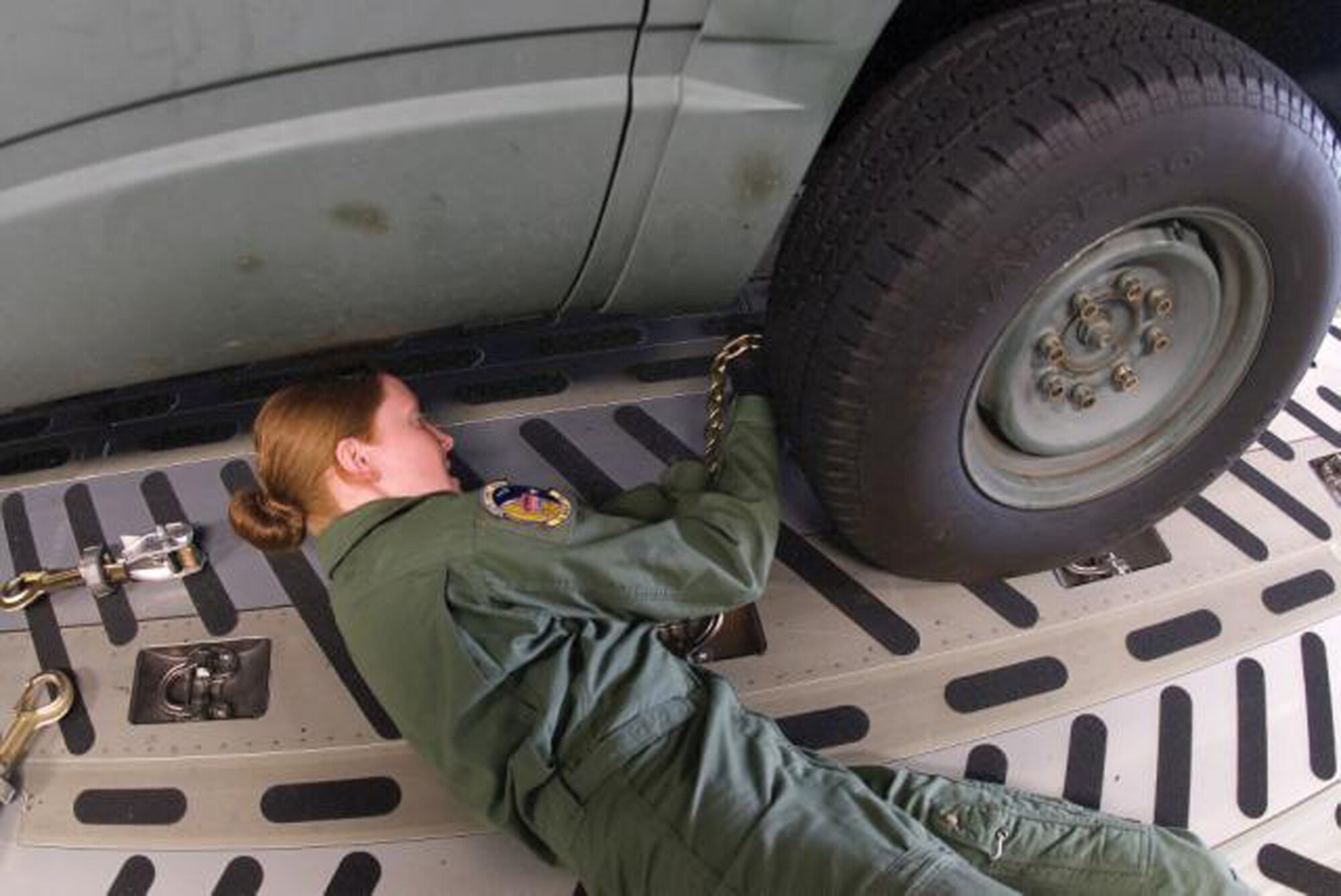 Airman 1st Class Jessica Narraway, 3rd Airlift Squadron C-17 loadmaster, chains down a vehicle to the cargo floor prior to departure.  (U.S. Air Force Photo / Roland Balik) 