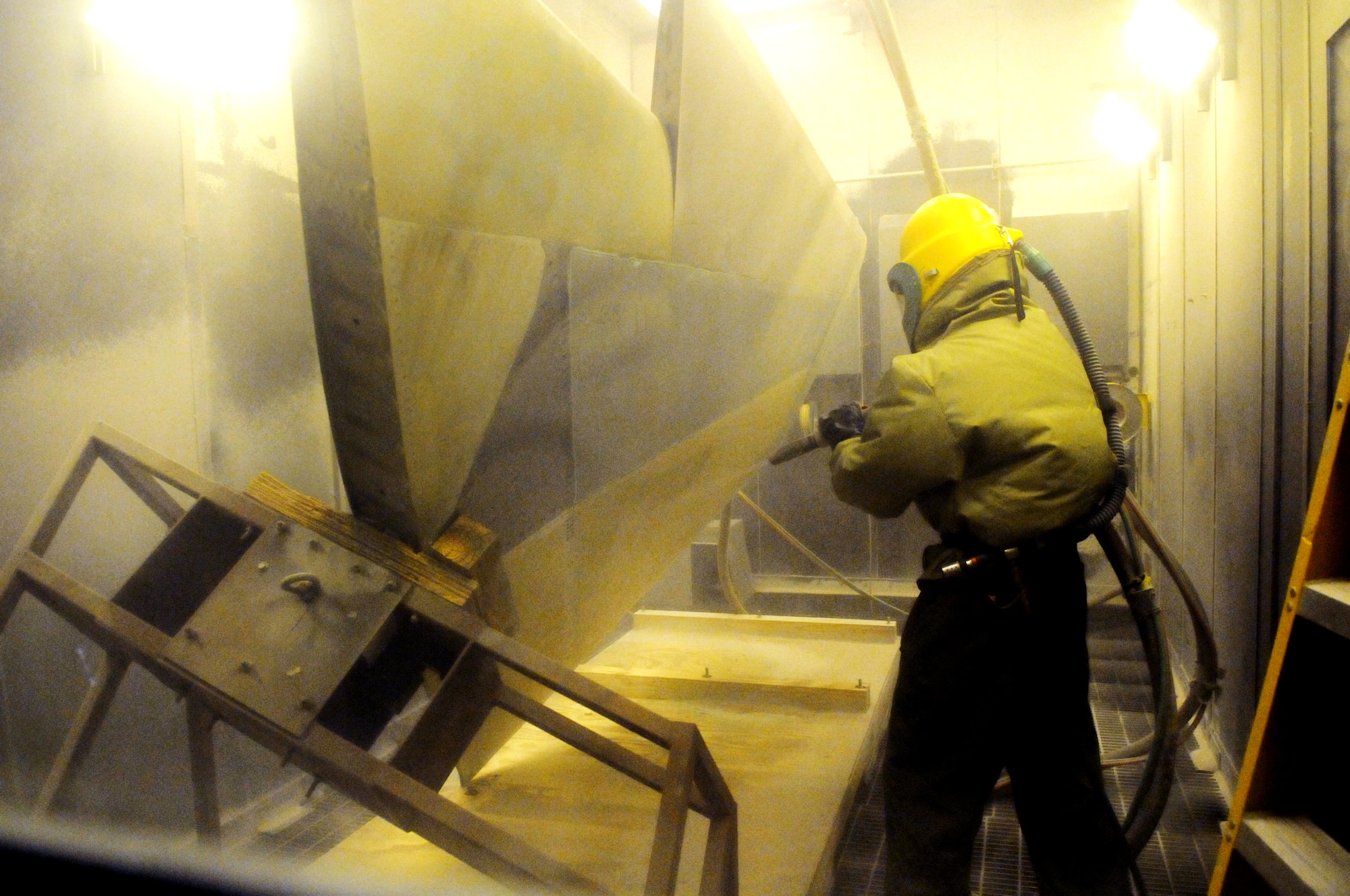 Willie Jolly works in a plastic media blaster booth cleaning an F-15 horizontal stab. He wears protective equipment and an air supply to work in the booth. U. S. Air Force photo by Sue Sapp