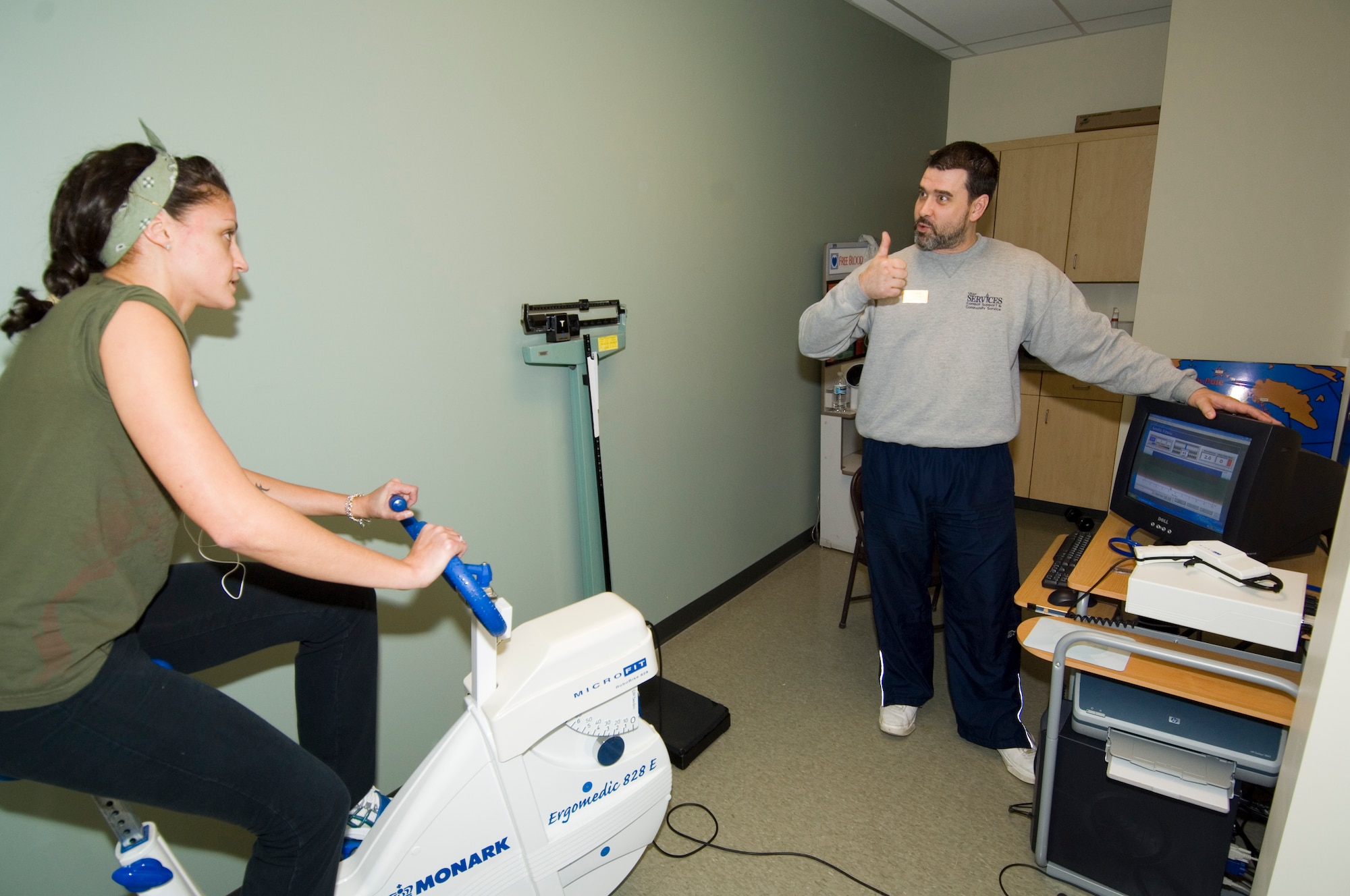 Kristen O’Connor rides a stationary bike as part of a comprehensive fitness assessment offered by the base Fitness Center while certified fitness trainer Paul Shoesmith monitors her progress.  Base fitness specialists recommend starting any exercise regimen with an initial assessment, and strongly encourage people to ask questions and seek advice about developing the right program for them.  (USAF Photo by Rick Berry)