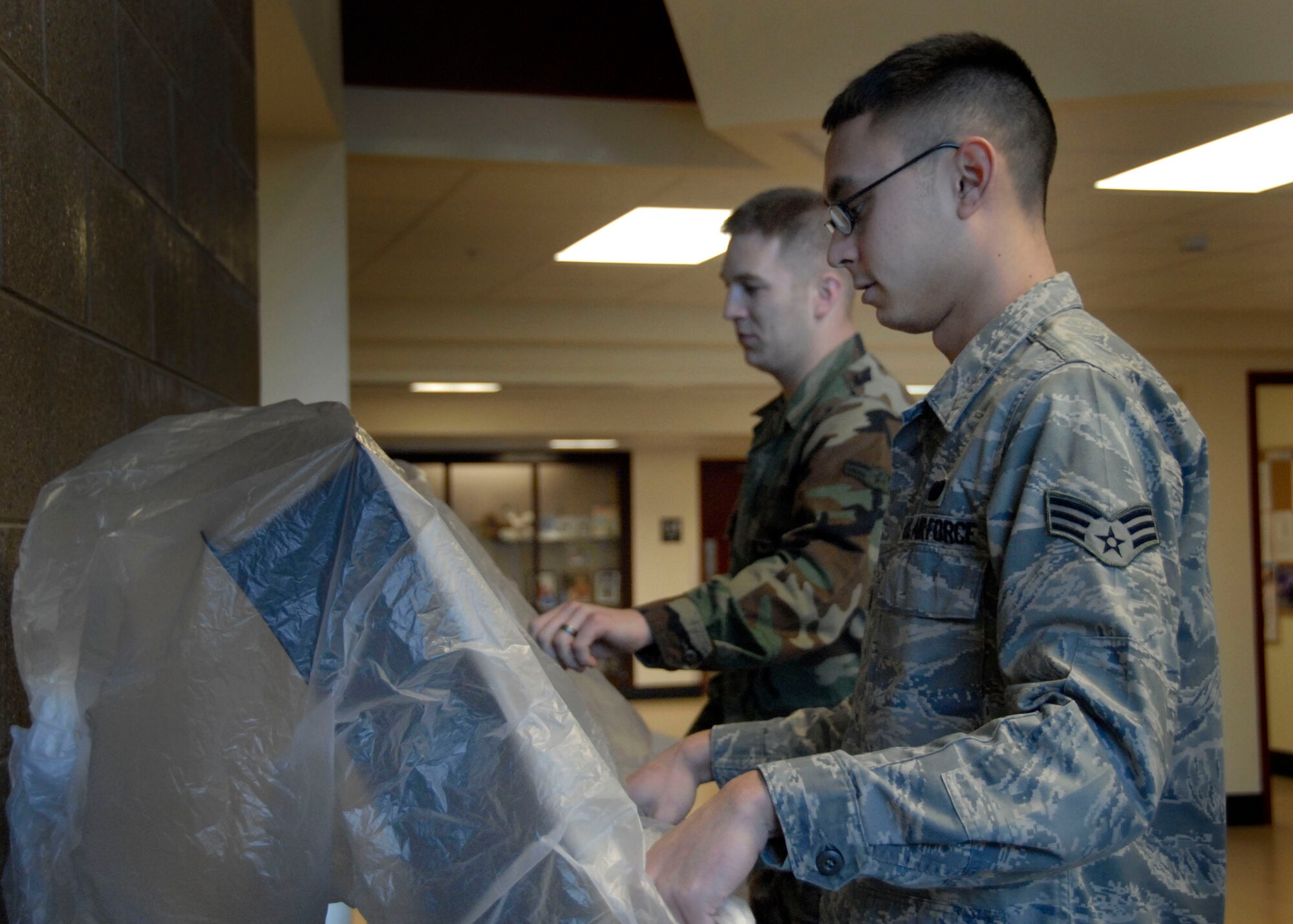 ELMENDORF AIR FORCE BASE, Alaska -- Senior Airman James Bruhl and Airman 1st Class Eric Dingus cover the Fitlinxx kiosks at the fitness center entrance Feb. 4, 2009. Arctic Warriors all over the base are protecting their shops electronics from possible ashfall that might occur if Mount Redoubt erupts. Airmen Bruhl and Dingus are fitness apprentices with the 3rd Services Squadron. (U.S. Air Force photo/Airman 1st Class Cynthia Spalding)