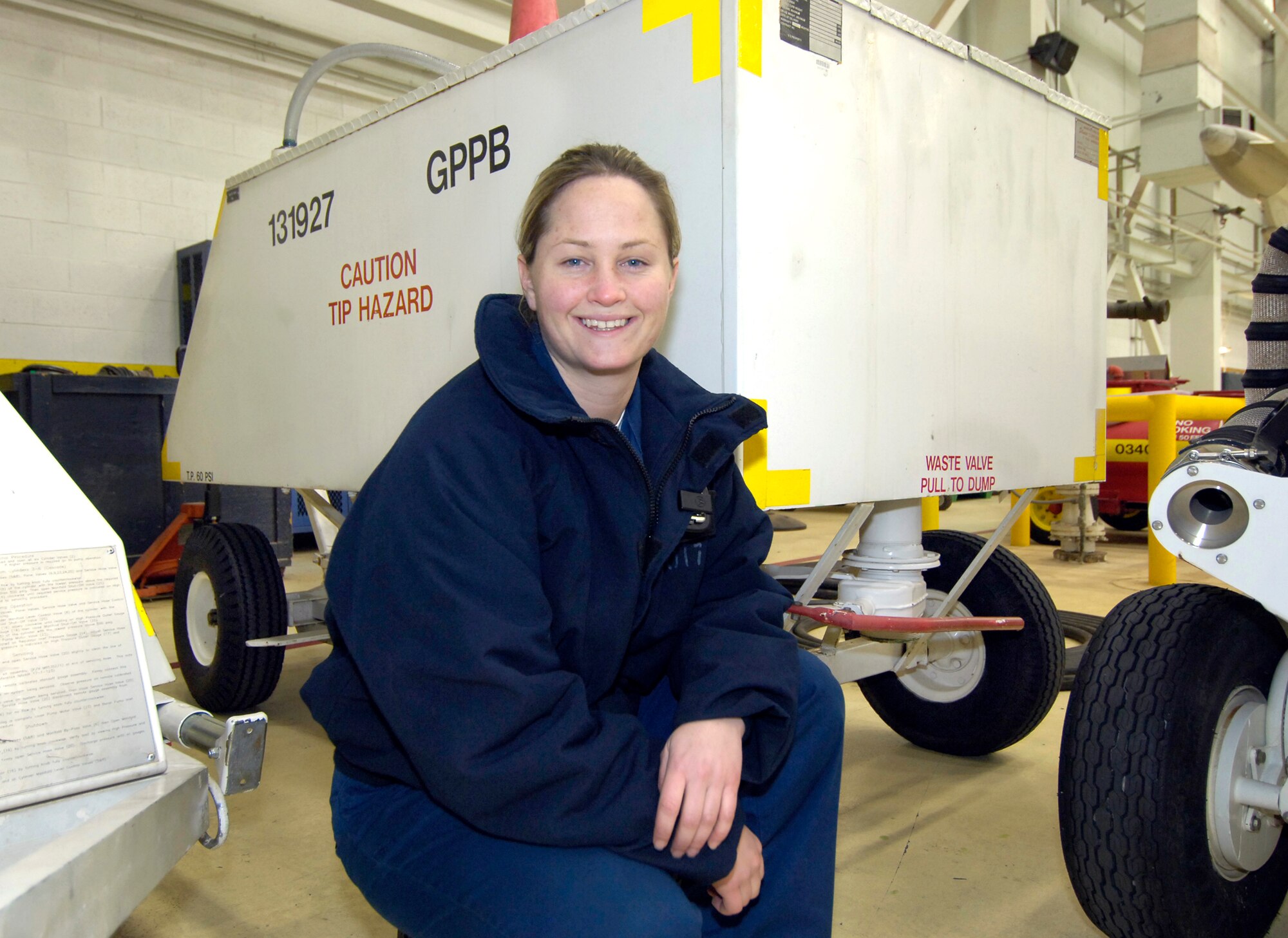 Working an aircraft’s lavatory cart is a job that may elicit sniggers from outsiders, but it’s a vital part of the work Navy Line Division personnel do to keep their jets ready to fly.  Petty Officer 3rd Class Ashley Cook, VQ-4, is one of those professionals who explained the job and the cart shown behind her. The two-person task is shared by an experienced maintainer and a rookie who clean out the jet’s seven-gallon tank every 24 hours or when the aircraft is maintained.  Wearing goggles, aprons, gloves, head protection and hearing protection, (masks are optional) the team hooks lines that will pump in a neon green mixture of water and glycol (keeps the water from freezing) after flushing the tank.  Tips for the rookie?  The cart is top heavy and easy to tip over.  The red handle on the end isn’t a cart brake; it opens the waste dump valve. And hook your lines up right.  If not, “It’s a bad day”, the petty officer said with a smile. (Air Force photo/Margo Wright)