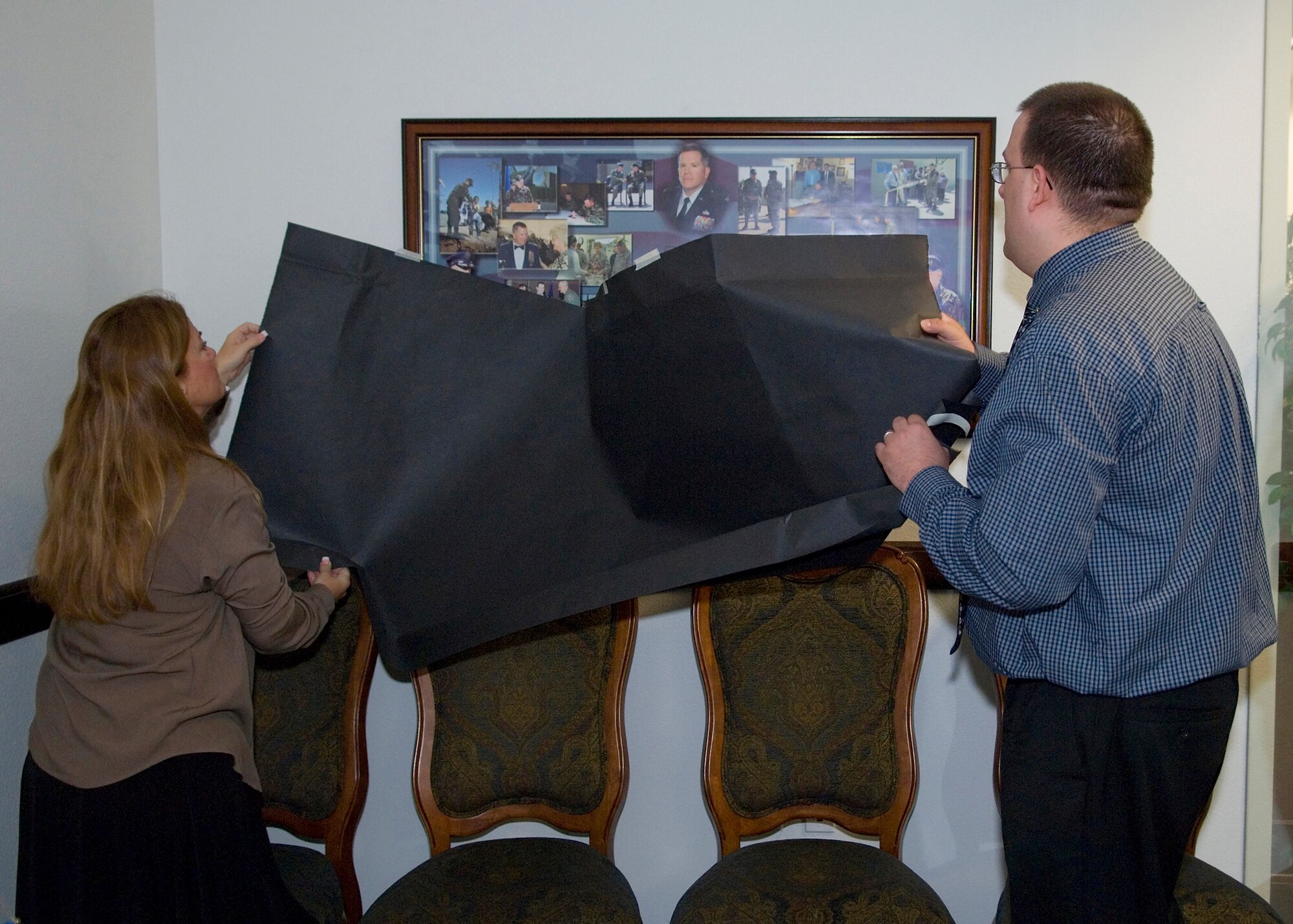 John Nichols (right), 95th Civil Engineer and Transportation Directorate executive assistant, and Susan Haseltine, 95th Air Base Wing plans and programs analyst, unveil the photo montage of Col. Bryan Gallagher during the colonel's memorial Feb. 5 at building 3000. Colonel Gallagher died after he was found unconscious at the Rosburg Fitness Center parking lot on Feb. 5, 2008. As part of the ceremony, a room in the 95 ABW Command Section was dedicated in his memory. (Air Force photo by Mike Cassidy)