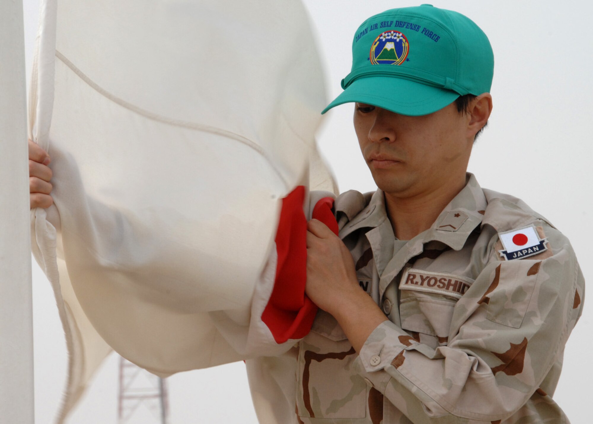 SOUTHWEST ASIA -- Japanese Staff Sgt. Ryu Yoshida, Japanese Air Self Defense Force Redeployment Group, grasps the Japanese flag as it is lowered for the last time at an air base in Southwest Asia, Feb. 10. Lowering the flag represents the end of the JASDF?s Iraq Reconstruction Support Airlift Wing Mission.  (U.S. Air Force photo/Senior Airman Courtney Richardson)