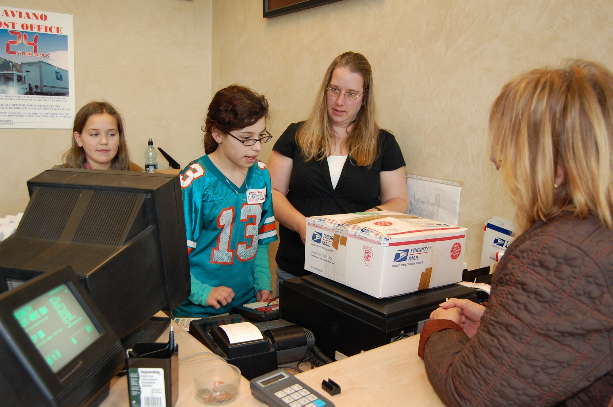 Heidi Spaulding, oversees Aviano Middle School students Kierianna Chavez (middle) and Bailey Spaulding as they assist a base post office customer Feb. 5. The students shadowed post office workers throughout the day as part of the school?s annual Job Shadow Day. Bailey is Ms. Spaulding's daughter. (U.S. Air Force photo/Staff Sgt. Lindsey Maurice)