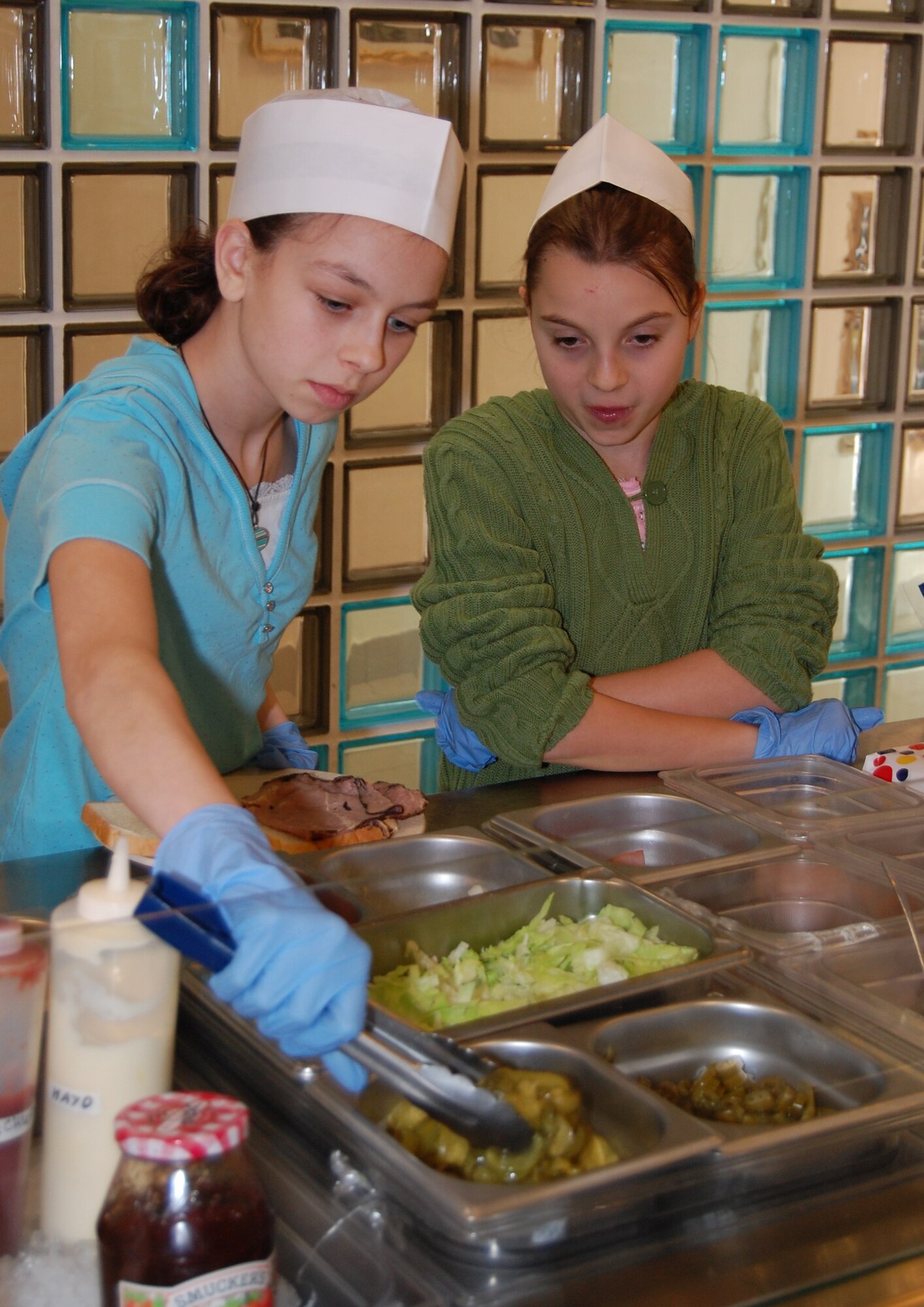 Aviano Middle School student Kayla Shoemaker watches as Sabrina Schweitzer adds pickles to a Buon Apetito Dining Facility customer's sandwich Feb. 5. Kayla and Sabrina, also an Aviano Middle School student, shadowed dining facility staff members during the school's annual Job Shadow Day. (U.S. Air Force photo/Staff Sgt. Lindsey Maurice)