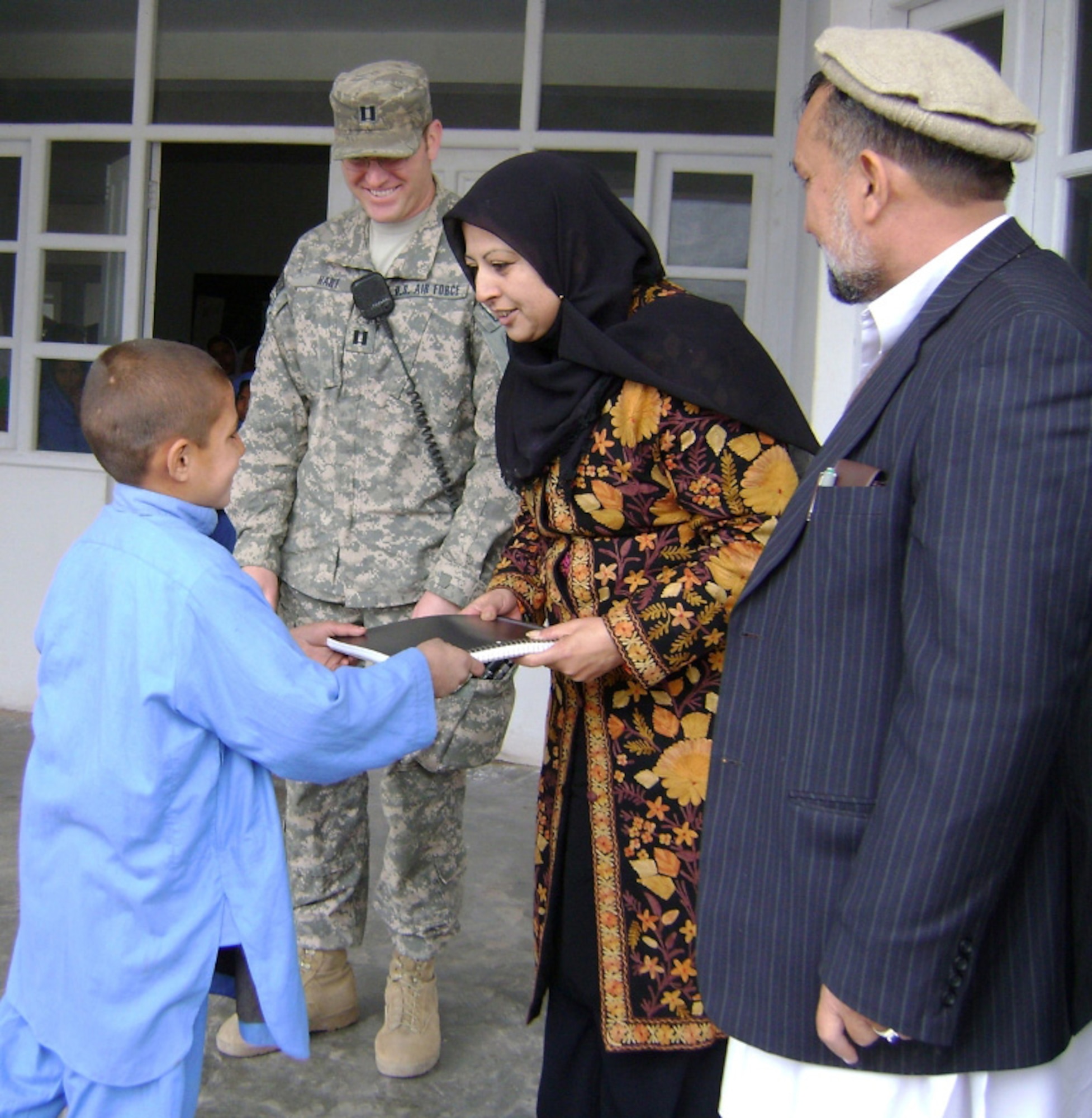 Mina Wali, Hope of Mother director, presents a notebook to a student for scoring the highest exam grade in his class, while U.S. Air Force Capt. Dustin Hart, Nangarhar Provincial Reconstruction Team, and Surkh Rod sub-governor Said Ali Akbar look on. The Hope of Mother School educates more than 400 students in the rural Sham Shapur village in Surkh Rod District. (U.S. Army courtesy photo)                               