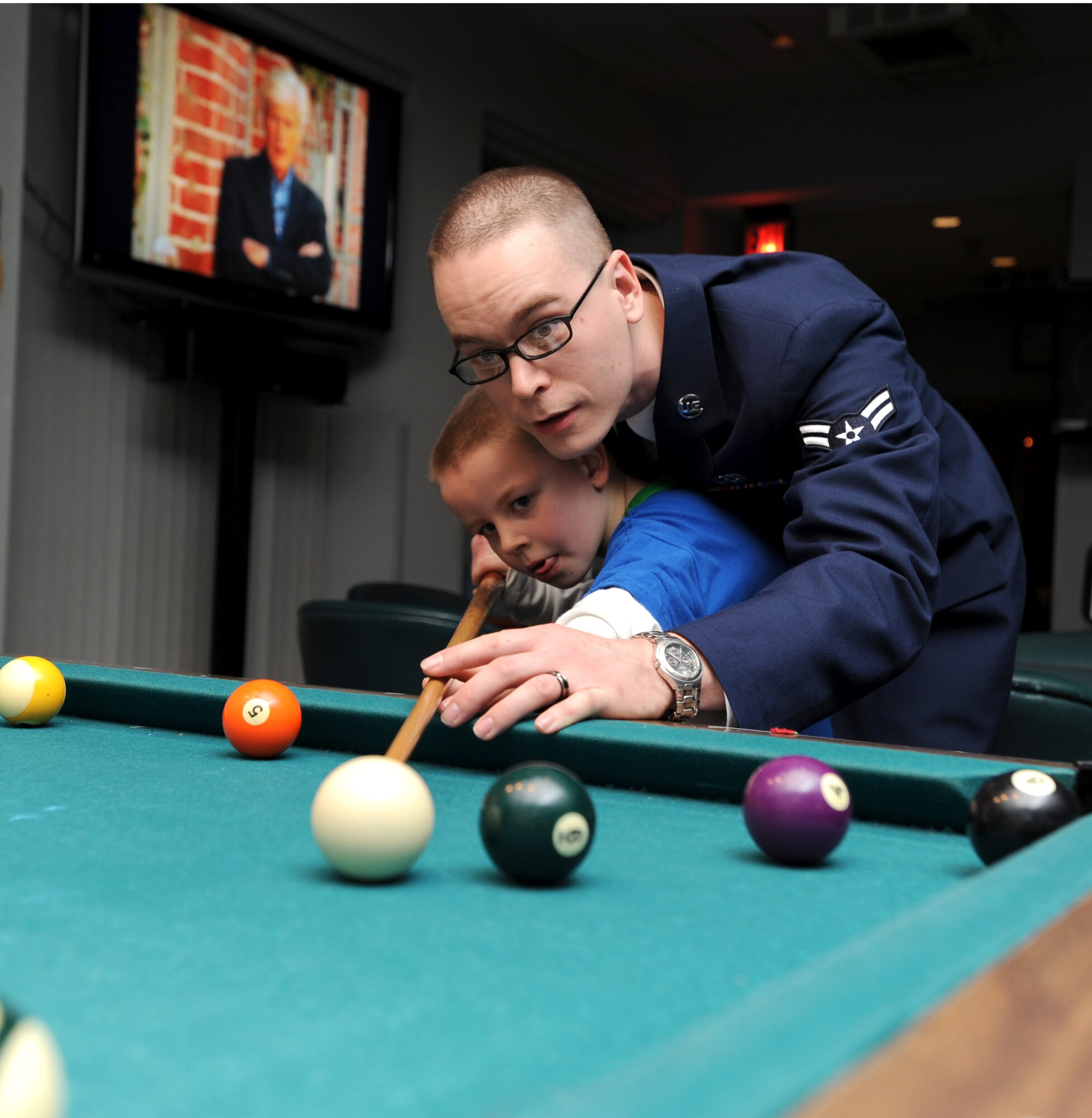 MCCONNELL AIR FORCE BASE, Kan. -- Airman 1st Class Richard Christensen, 22nd Maintenance Operation Squadron, helps his son Richard, 7, line up a shoot during a pool game for First Friday at the Storm Cellar, Feb 6. First Friday is held on the first Friday of the month from 9 p.m. to 1 a.m. and it gives Airmen an alternative to going off base for entertainment. These events will be having live music starting in March and are open to all ages.   (Photo by Senior Airman Roy Lynch) 