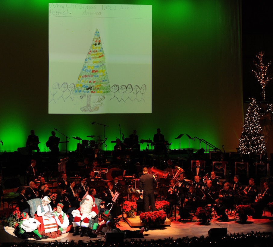 Members of Concert Band along with Mr. and Mrs. Claus perform 'Why Christmas Trees Aren't Perfect' during the USAF Heartland of America Band's Holiday Show "The Promise of the Season."  Also pictured in the background is an example of artwork submitted by local schools to help illustrate the story.
