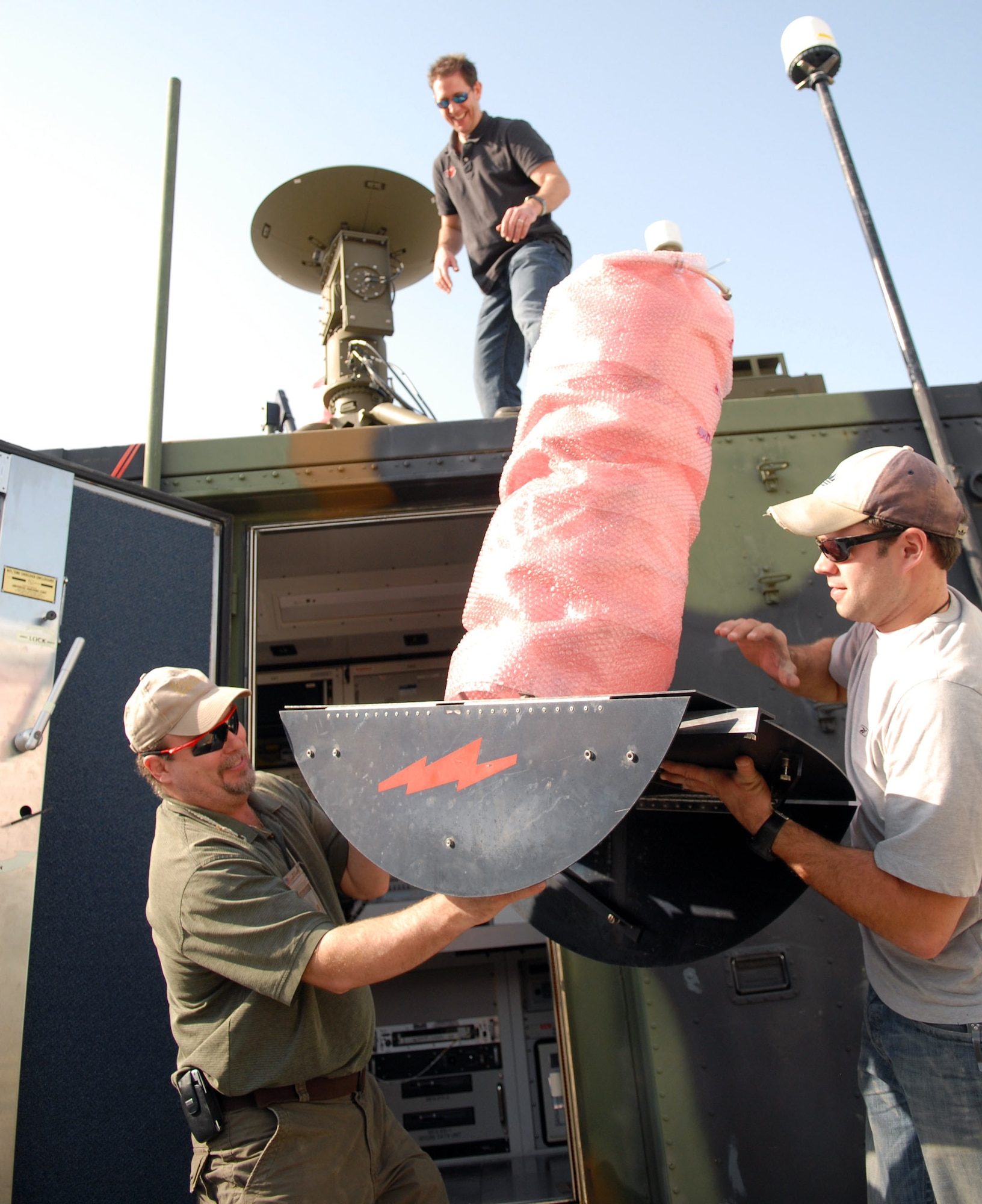 Eddie Evans (left) and Troy Rappleye hand an ultrahigh frequency satellite antenna to Michael Williams that is being installed at an airbase in Southwest Asia.  The antenna will provide a wideband link to the Navy's first Global Hawk in the area of operations.  Mr. Rappleye and Mr. Williams are field support representatives for L3 Communications, while Mr. Evans is an aircraft ground technician with Northrop-Grumman.  (U.S. Air Force photo/Tech. Sgt. Denise Johnson)