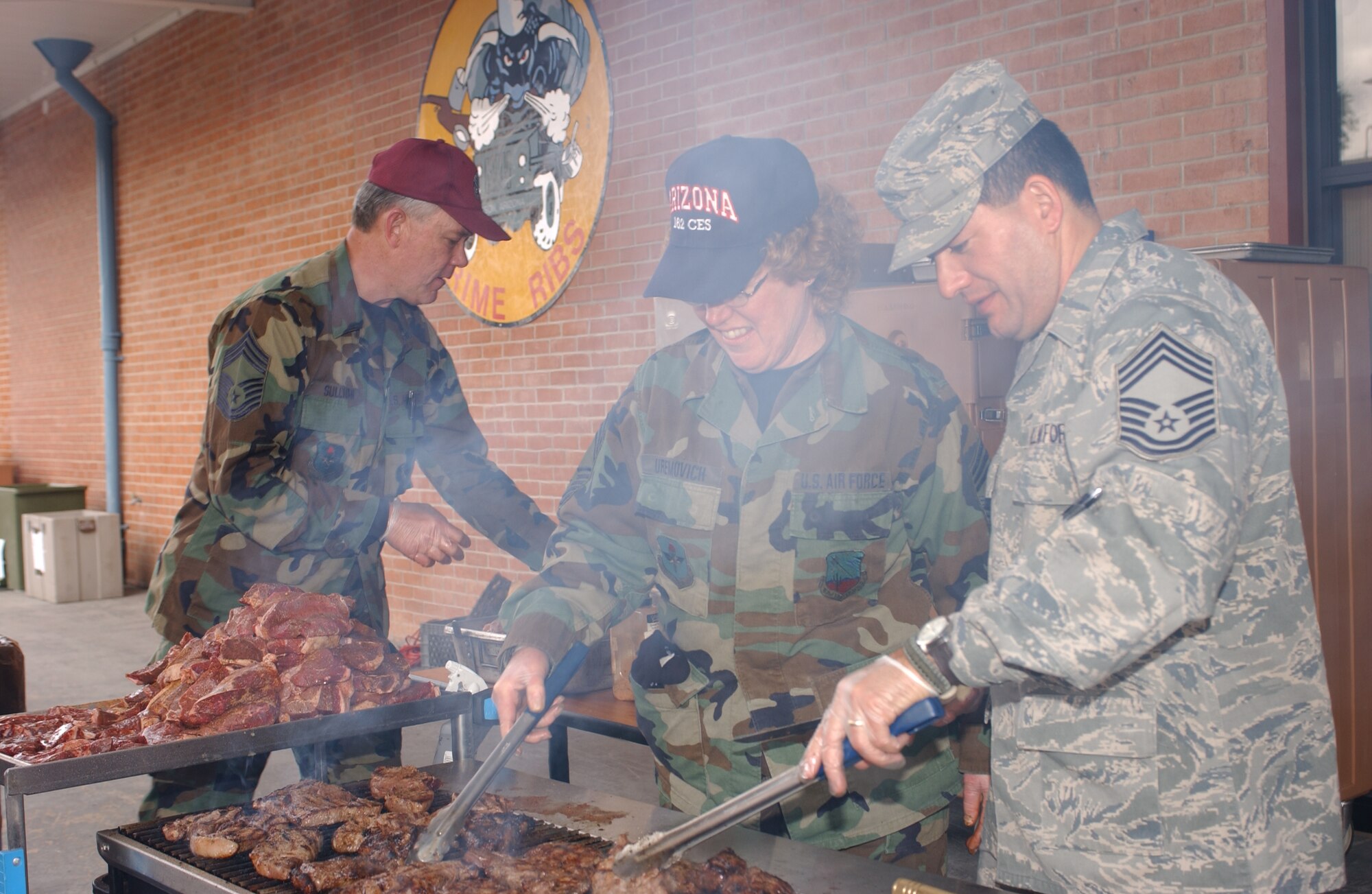 (From left to right) Chief Master Sgts. Russell Sullivan, Nikki Uremovich and George Silvas grill steaks in front of the Desert Rose Dining Facility for the wing’s annual Steak Fry event, Feb. 7. (Air National Guard photo by Senior Airman Sara Elliott)