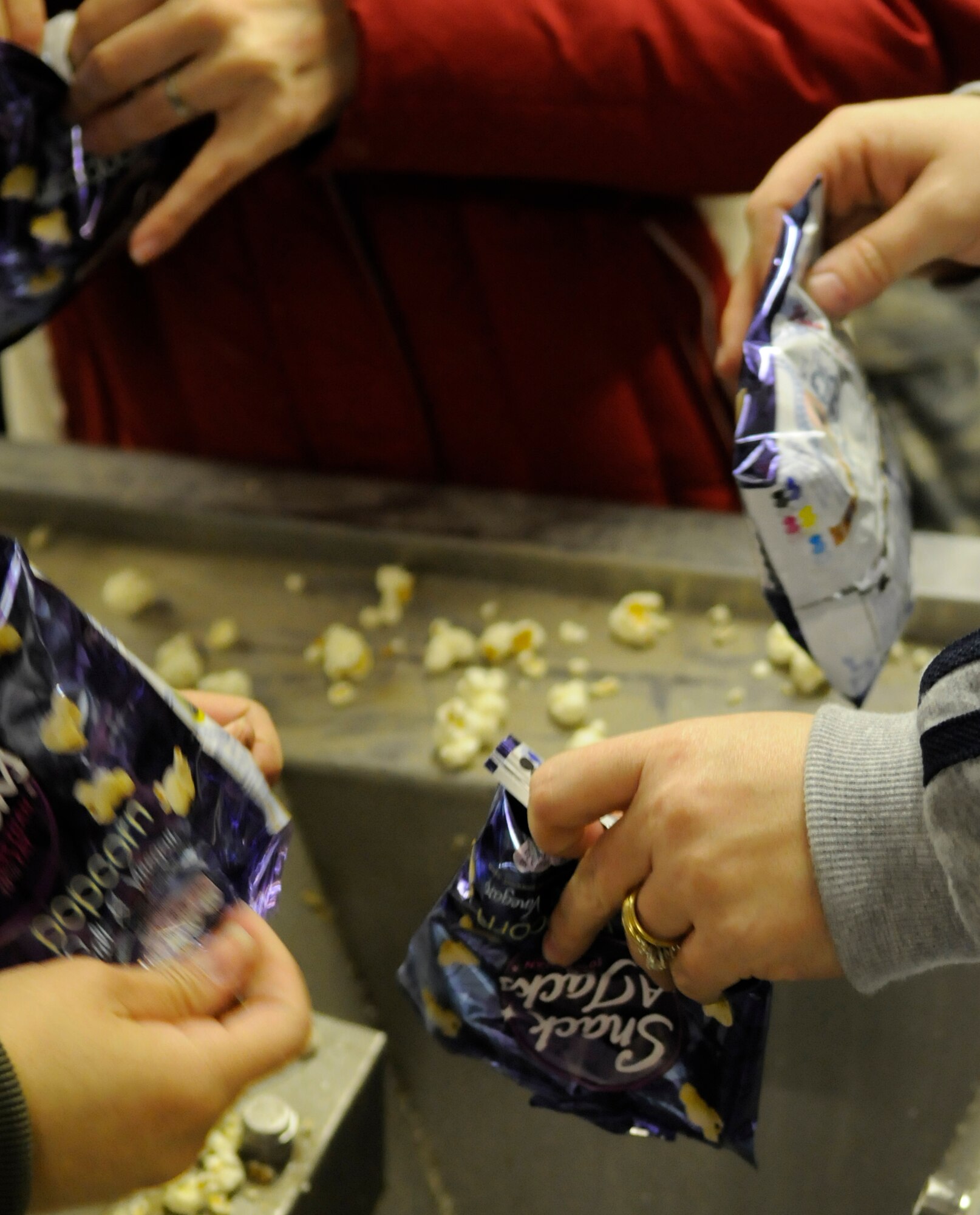 Staff Sgt. Sarah Stacy-Smith, 352nd Operations Support Squadron (upper right),  Staff Sgt. Lisa Patsios (upper left) and Senior Airman Leticia Elias (lower left) both from the 488th Intelligence Squadron, empty out-of-date popcorn from snack bags to be used as cattle feed for a less-fortunate family at the Newmarket Open Door, a charitable organization in Newmarket, England, Feb 6, 2009.  The members of Team Mildenhall 5/6 were three of nine who volunteered their time to help the needy and build community ties with the British population.(U.S. Air Force photo by Senior Airman Christopher L. Ingersoll)