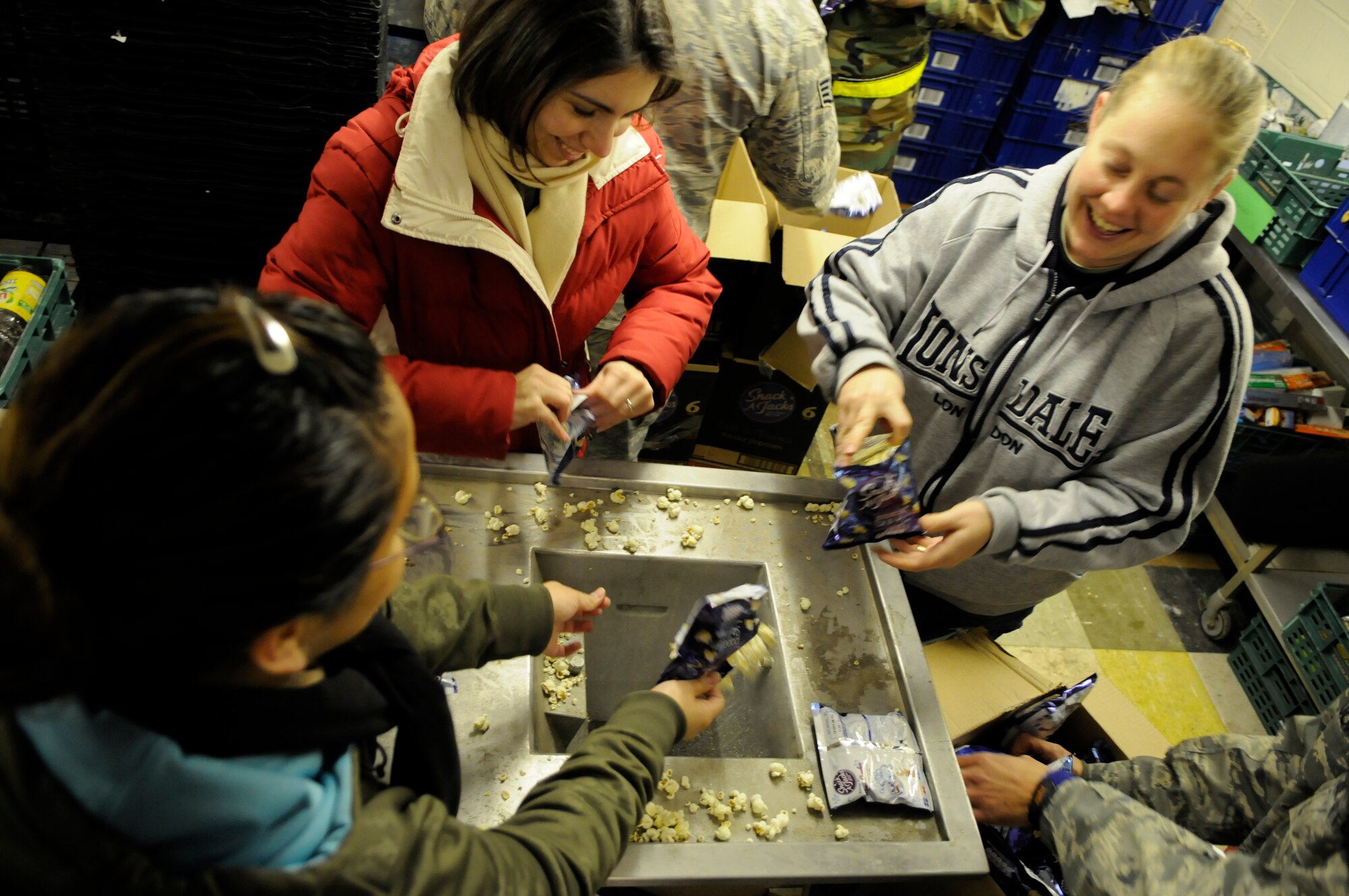 Staff Sgt. Sarah Stacy-Smith, 352nd Operations Support Squadron (upper right),  Staff Sgt. Lisa Patsios (upper left) and Senior Airman Leticia Elias (lower left) both from the 488th Intelligence Squadron, empty out-of-date popcorn from snack bags to be used as cattle feed for a less-fortunate family at the Newmarket Open Door, a charitable organization in Newmarket, England, Feb 6, 2009.  The members of Team Mildenhall 5/6 were three of nine who volunteered their time to help the needy and build community ties with the British population.(U.S. Air Force photo by Senior Airman Christopher L. Ingersoll)