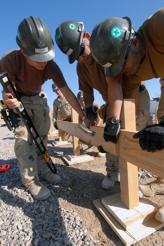 U.S. Navy Petty Officer 2nd Class Jeffrey Roberts, left, and Seaman Michael Joseph, right, hold a board in place while Petty Officer 2nd Class Joaquin Quintero, nails it down while working on a foundation at a patrol base in Mahawil, Iraq, Feb. 4, 2009.