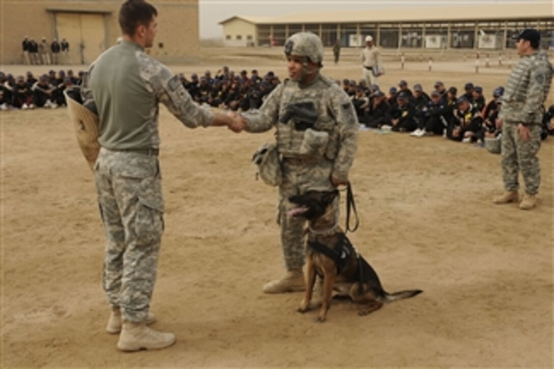 U.S. Army Sgt. Tyler Barriere (left) of the 2nd Special Troops Battalion, 2nd Brigade Combat Team, 4th Infantry Division shakes hands with Sgt. Troy Stiner to demonstrate that Ruby, a military working dog assigned to Stiner, will not attack an innocent bystander during a demonstration at the Diwaniyah Police Academy in Diwaniyah, Iraq, on Feb. 9, 2009.  The soldiers also conducted an assessment of the academy to ensure they are getting the supplies they need.  