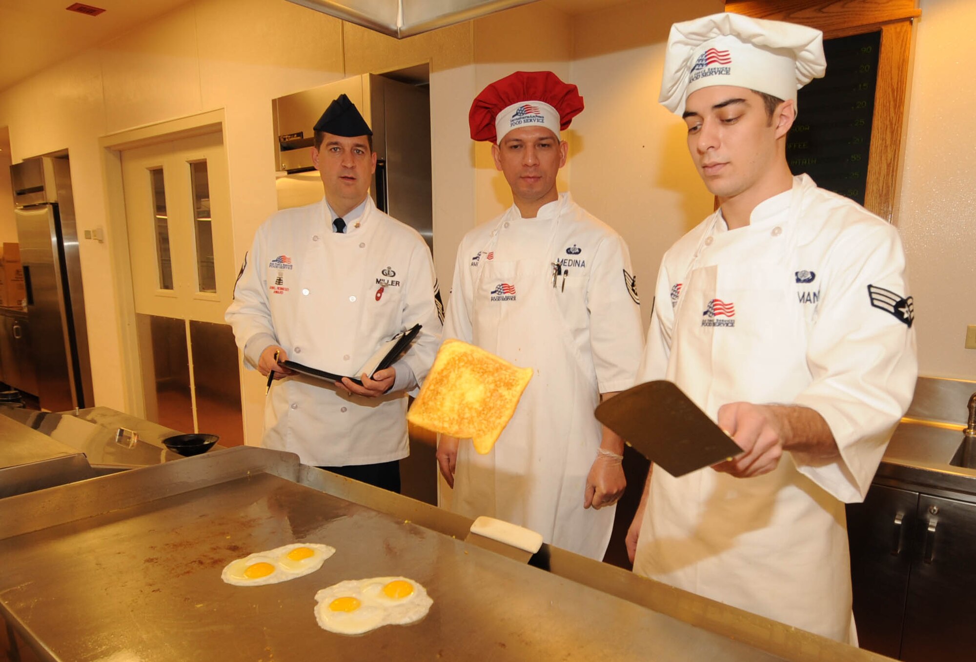 Senior Airman Matthew Baumann, 92nd Force Support Squadron food service journeyman, flips a French toast as Tech. Sgt. Adrian Medina, 92nd Force Support Squadron Air Force chef, and Senior Master Sgt. Troy Miller, HQAFSVA supervisor of plans and programs, San Antonio, Texas, evaluates culinary skills. (U.S. Air Force photo / Staff Sgt. JT May III)