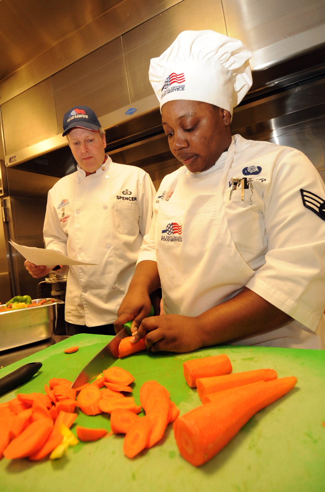 Senior Airman Riquette Wynter, 92nd Force Support Squadron food service journeyman, cuts vegetables on the cutting board while Bill Spencer, Headquarters Air Force Services Agency chief food and beverage support branch inspector, watches. Mr. Spencer is a member of a four-man inspection team known as the Hennessey team stationed at San Antonio, Texas. This group inspects the best food services in the Air Force. The inspection took place Feb. 12 to 14 at the Ross and Warrior dining facilities.(U.S. Air Force photo / Staff Sgt. JT May III)