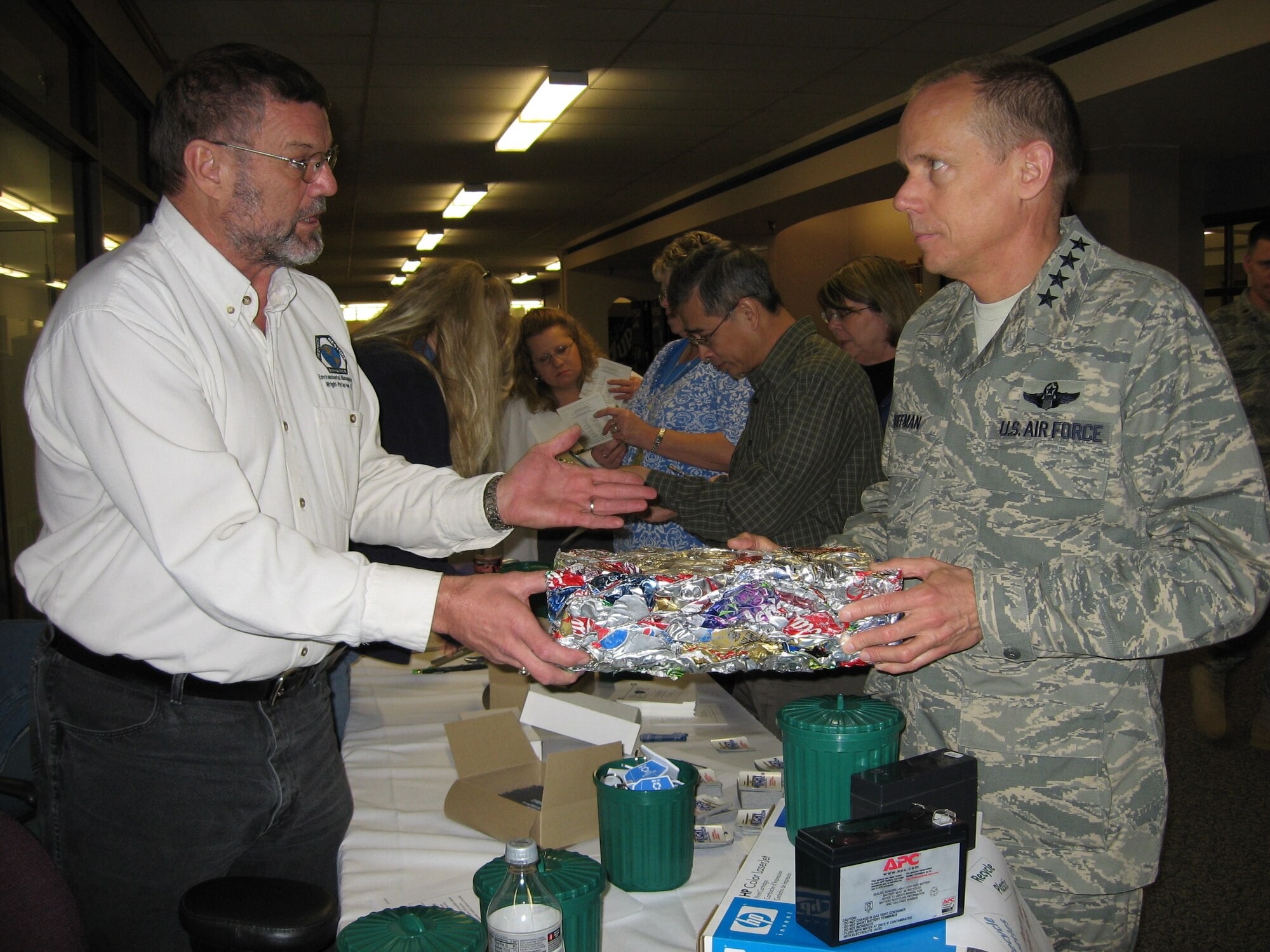 WRIGHT-PATTERSON AFB, Ohio -- Clad in a shirt made of 50 percent recycled milk jugs, Bill Meinerding shows off a block of crushed aluminum cans to Gen. Donald Hoffman, Air Force Materiel Command commander.  Mr. Meinerding and Cathy Hillard from the 88th ABW Qualified Recycling Program set up shop Thursday in the AFMC headquarters building to talk about the methods and benefits of recycling. The display included pencils made of old denim and worn-out paper currency; miniature trash cans to encourage reducing waste; and smoothed ground-up glass that can be used for mulch and garden walkways. With resources conservation as one of his top priorities, General Hoffman made it a point to visit the booth and learn more about recycling efforts on base.  For example, Mr. Meinerding told General Hoffman it takes about 600 crushed cans to form a 20 pound block of aluminum, similar to the one pictured. The blocks are then sold to companies and are typically used to make more cans. (Air Force photo by Ron Fry)