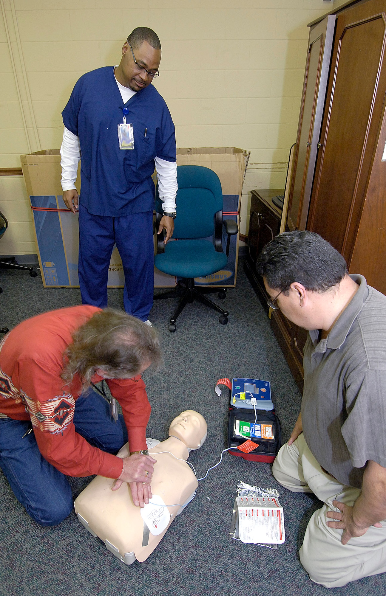 Marcus Brown watches Steve Gregory, left, and Ernie Maldonado, both of the 448th Supply Chain Management Wing, practice CPR and use an  Automated External Defibrillator during a recent training class.  Mr. Brown helps train Tinker personnel on using the AED’s, 255 of which are located in 74 buildings across base. “The goal of quarterly training is to help eliminate panic,” said Mr. Brown, the public access defibrillation coordinator. (Air Force photo/Margo Wright)
