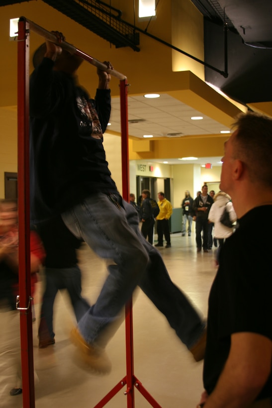 A passer-by takes the Marine Corps Pull-Up Challenge under the supervision of a Marine Feb. 21 at the George Mason University Patriot Center. Crowds of patrons scurried by the Marines booth at Ultimate Warrior Challenge 5, some of them stopping to win prizes for pull-ups.