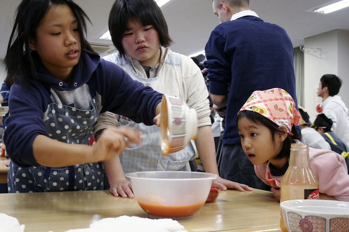Mai Yanagihara, a clerk at the Marine Mart seven day store, helps foster children spice buffalo wings during a cook-off at the Yahata Gakuen foster home in Hiroshima Feb. 21. Community members like Yanagihara also volunteered their time at the foster home alongside the Marines.