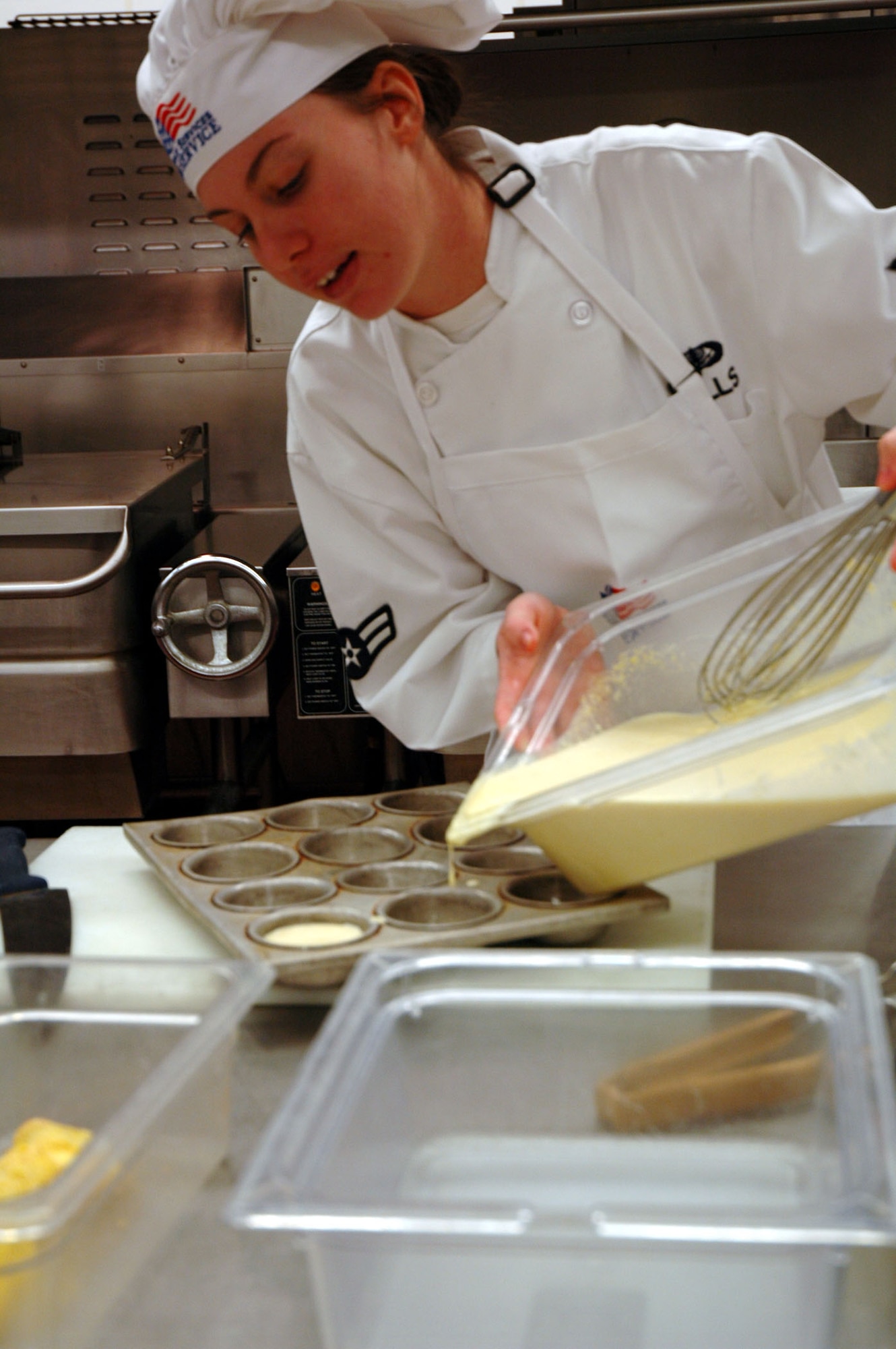 Airman 1st Class Lynsey Mills pours cornbread mix into greased muffin tins to be baked as a side dish to accompany her team's Catfish with Okra and Tomatoes entree in the annual Warrior Chef competition Feb. 19. (U.S. Air Force photo/Valerie Mullett)