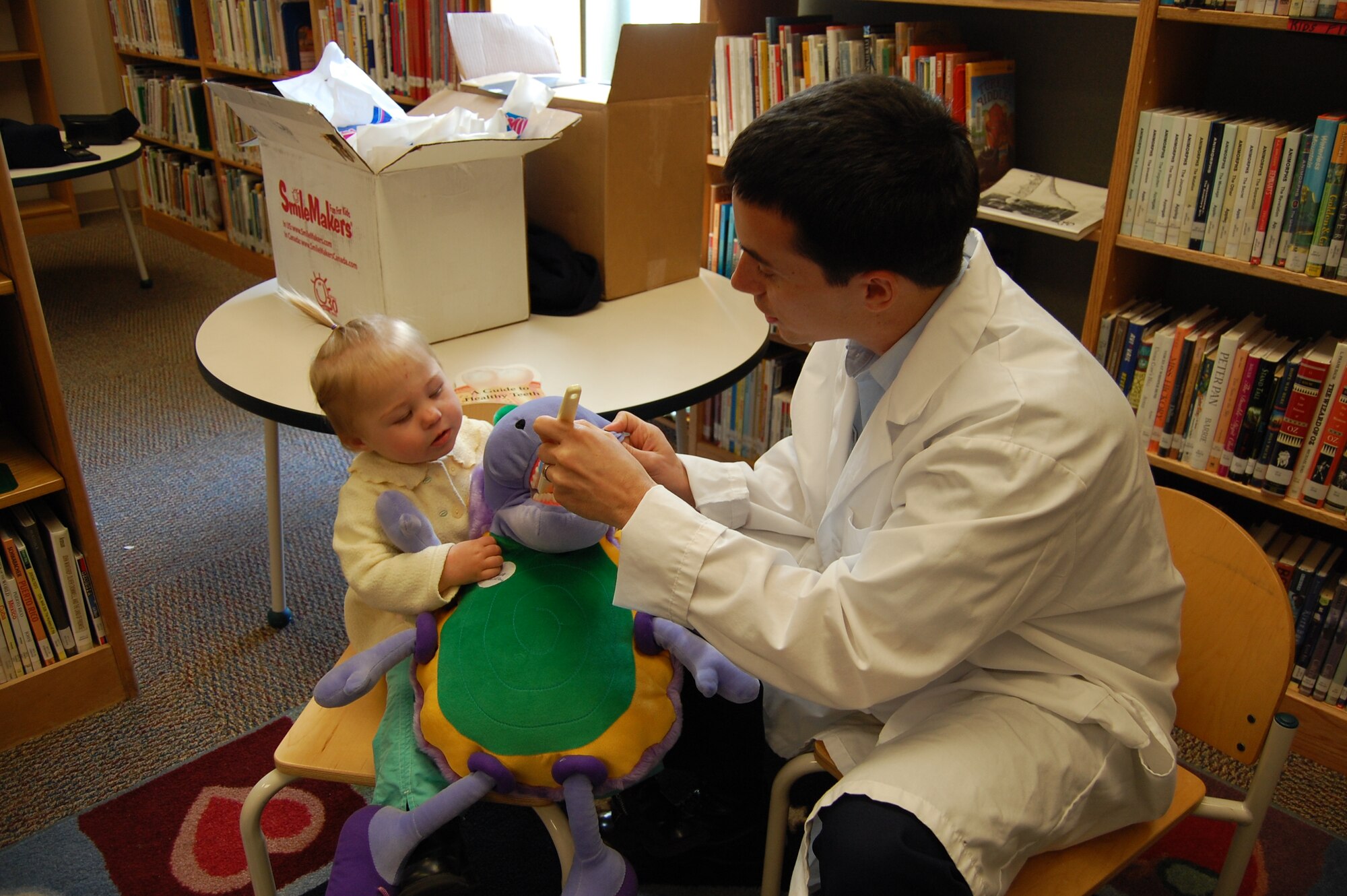 Staff Sgt. Jason Ware, 81st Dental Squadron dental technician, helps Adeline Streeter brush “Bugsy Malone’s” teeth Monday at McBride Library in observance of National Children’s Dental Health Month.  The 1-year-old’s parents are 2nd Lt. John and Emily Streeter, 81st Inpatient Operations Squadron. Tech. Sgt. Caroline Bunce, a registered dental hygienist, brought the puppet to demonstrate healthy dental habits, and special story times and projects emphasized dental health.  (U.S. Air Force photo by Steve Pivnick)
