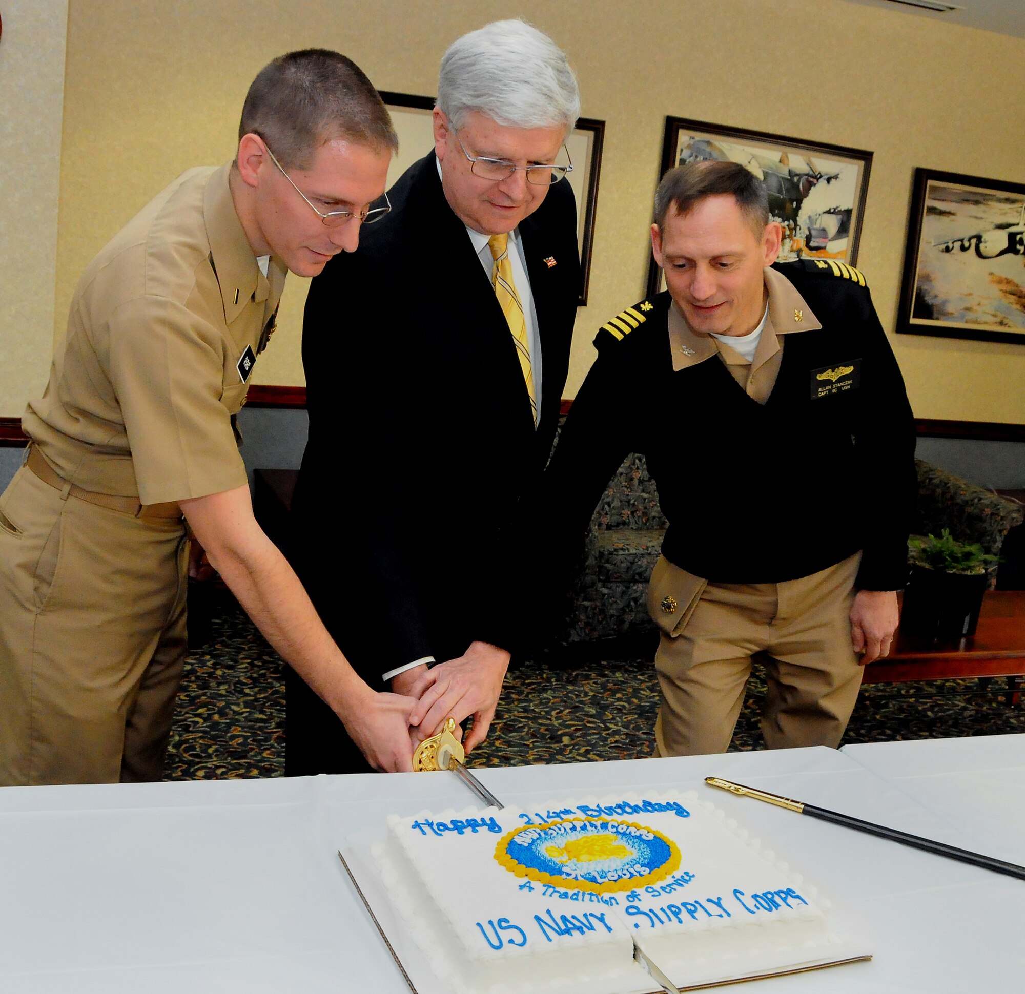 SCOTT AIR FORCE BASE, Ill. -- Lieutenant J.G. Quentin Lease of Military Surface Deployment and Distribution Command, retired Vice Adm. Keith Lippert and Capt. Allan Stanczak of  U.S. Transportation Command cut a cake Feb. 20 in celebration of the Supply Corps’ 214th birthday.  Mr. Lippert was the 41st chief of the Supply Corps from 1997 to 1999. The Saint Louis Area Supply Corps Association was established Jan. 5 this year and is comprised of 37 Supply Corps officers in the St. Louis area.  Members range in rank from ensign to two-star admiral. Primary commands represented are USTRANSCOM, SDDC and the Defense Contracting Management Agency/Boeing, St. Louis. The organization hosted its first official luncheon Feb. 20 at the USTRANSCOM in celebration of the Supply Corps' 214th Birthday. (Photo by Bob Fehringer)