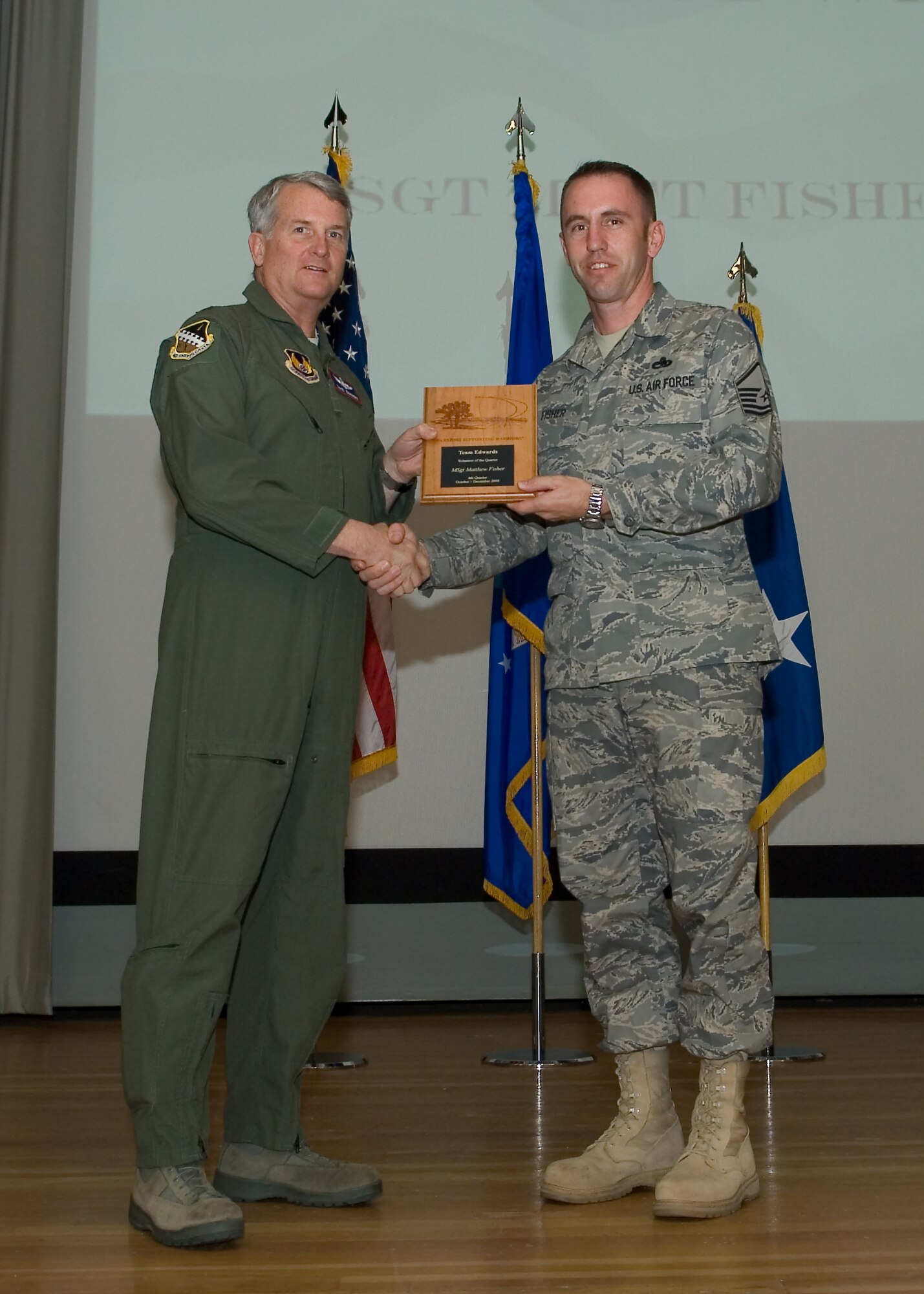 Maj. Gen. David Eichhorn (left), Air Force Flight Test Center commander, presents Master Sgt. Matthew Fisher, 412th Aircraft Maintenance Squadron with the Volunteer of the Fourth Quarter award during a ceremony at the base theater Feb. 24. (Air Force photo by Mike Yncera)
