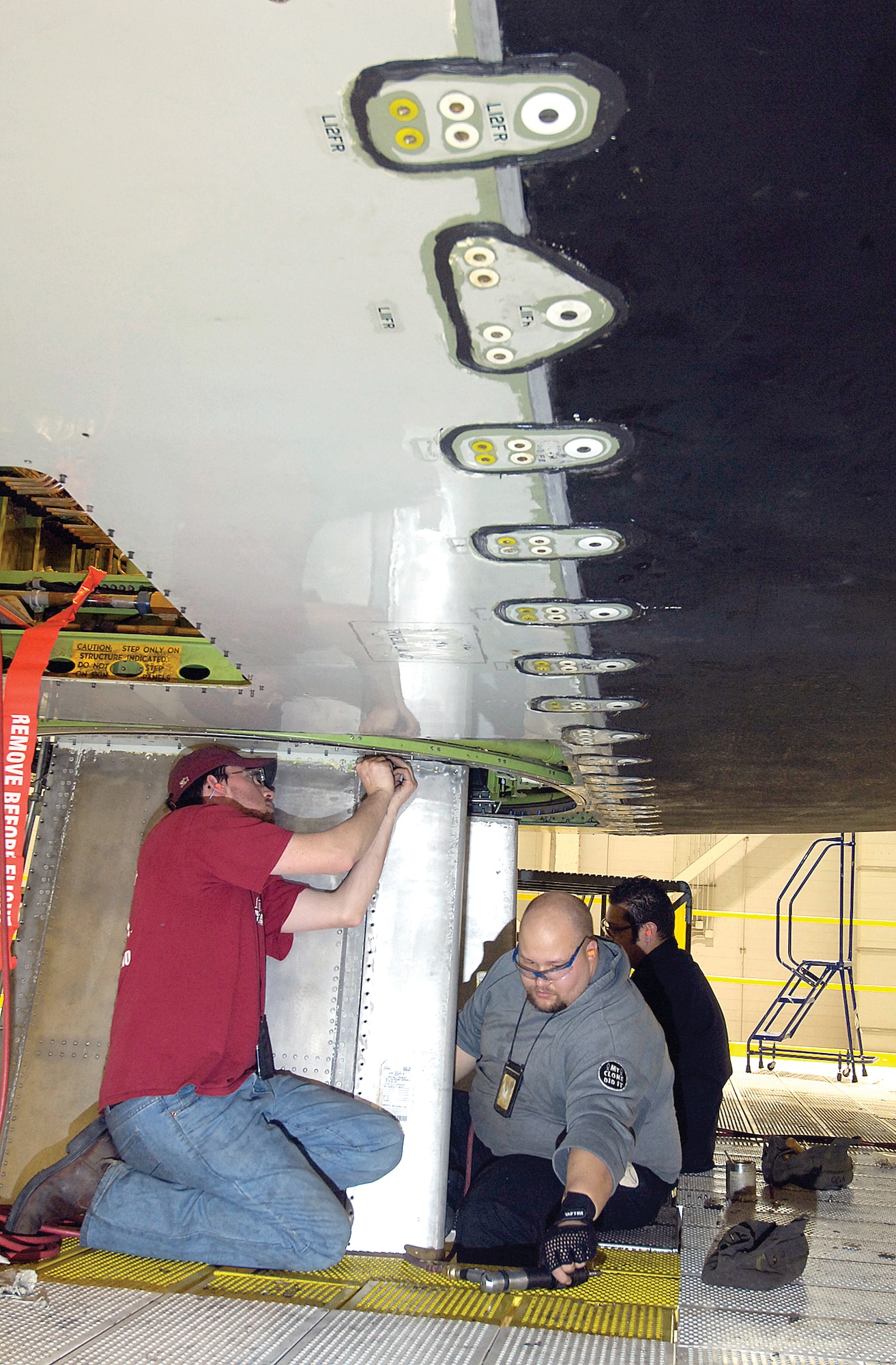 Working underneath the rotodome of an E-3 Sentry undergoing maintenance, aircraft mechanics Richard Todd, Russell Murphy and Jeremiah Petricek, from left, install pedestal farings. (Air Force photo/Margo Wright)