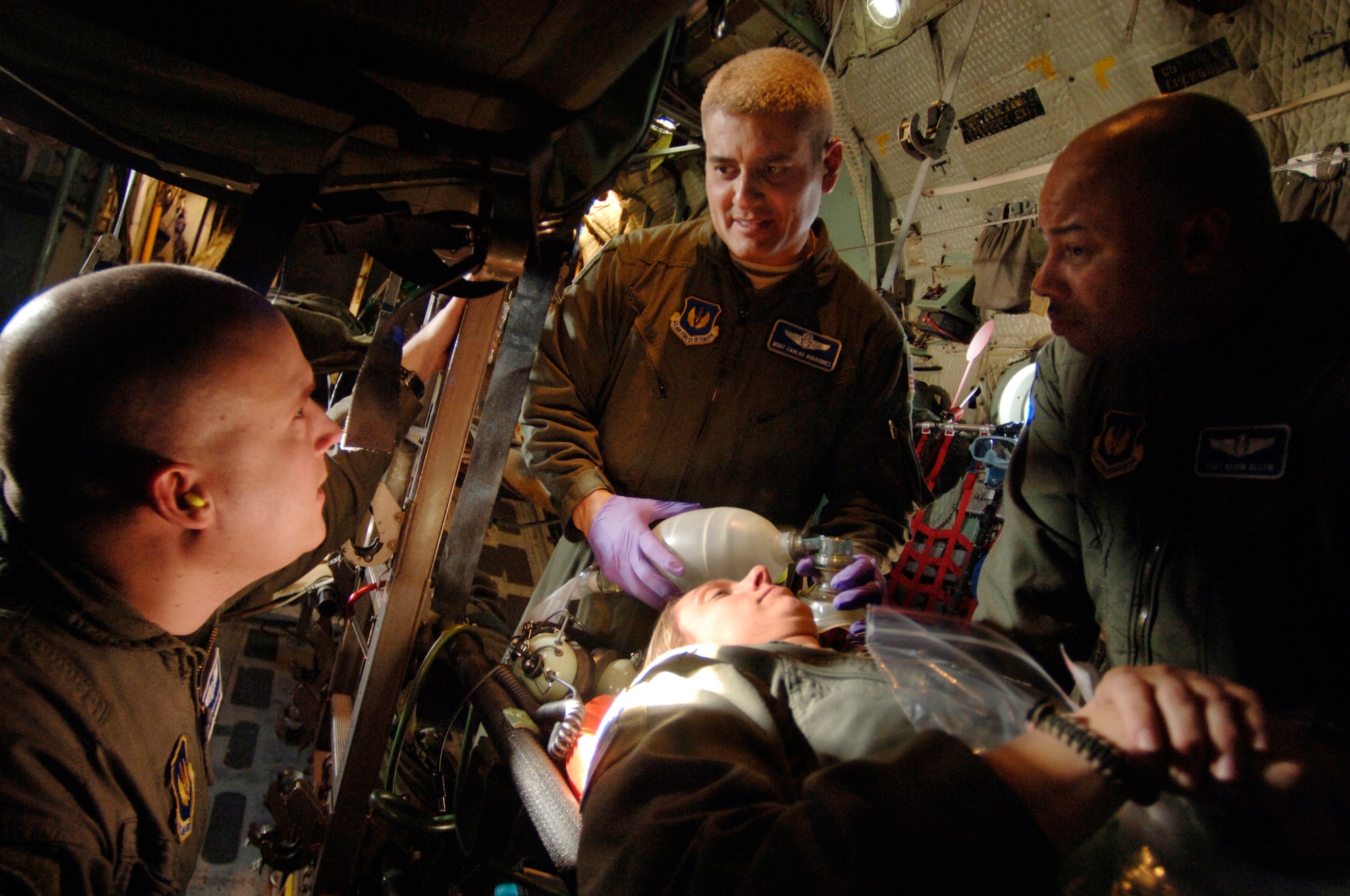 During an aeromedical evacuation training sortie on a C-130 Hercules flying over southern Germany, Tech. Sgt. Tommy Mattox (center), aerospace medical technician, describes symptoms of an anaphylactic shock "patient" to fellow healthcare providers Master Sgt. Carlos Rodriguez (left) and Tech. Sgt. Kevin Allen (right) who, along with a cadre of flight nurses, were being evaluated on the speed and quality of patient care., Capt. Stephanie Ellenburg, flight nurse instructor who is playing the role of the patient, was also evaluating the response of the medical team. The flight-qualified healthcare providers, assigned to the 86th Aeromedical Evacuation Squadron, fly weekly with Ramstein's 37th and 38th Airlift Squadron's C-130 fleet to remain proficient in their skills.  (Department of Defense photo by Master Sgt. Scott Wagers)