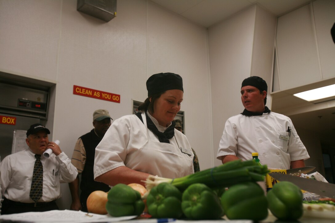 Tamara Zoria, 40, Vista, Calif., and Andrew Rude, 29, Fallbrook, Calif., food service cooks for Sodexo inspects the ingredients for the Culinary Team of the Quarter Competition here Feb. 25. The competition had a Mardi Gras celebration theme and each team had to prepare a full-course meal while maintaining that theme. The winners were awarded embroidered chef?s coats, gold medals, a plaque and a two-week trip to the Culinary Institute of America in New York. Marine Corps Air Station Yuma?s team came in first place and the team from Marine Corps Air Ground Combat Center Twentynine Palms came in second.