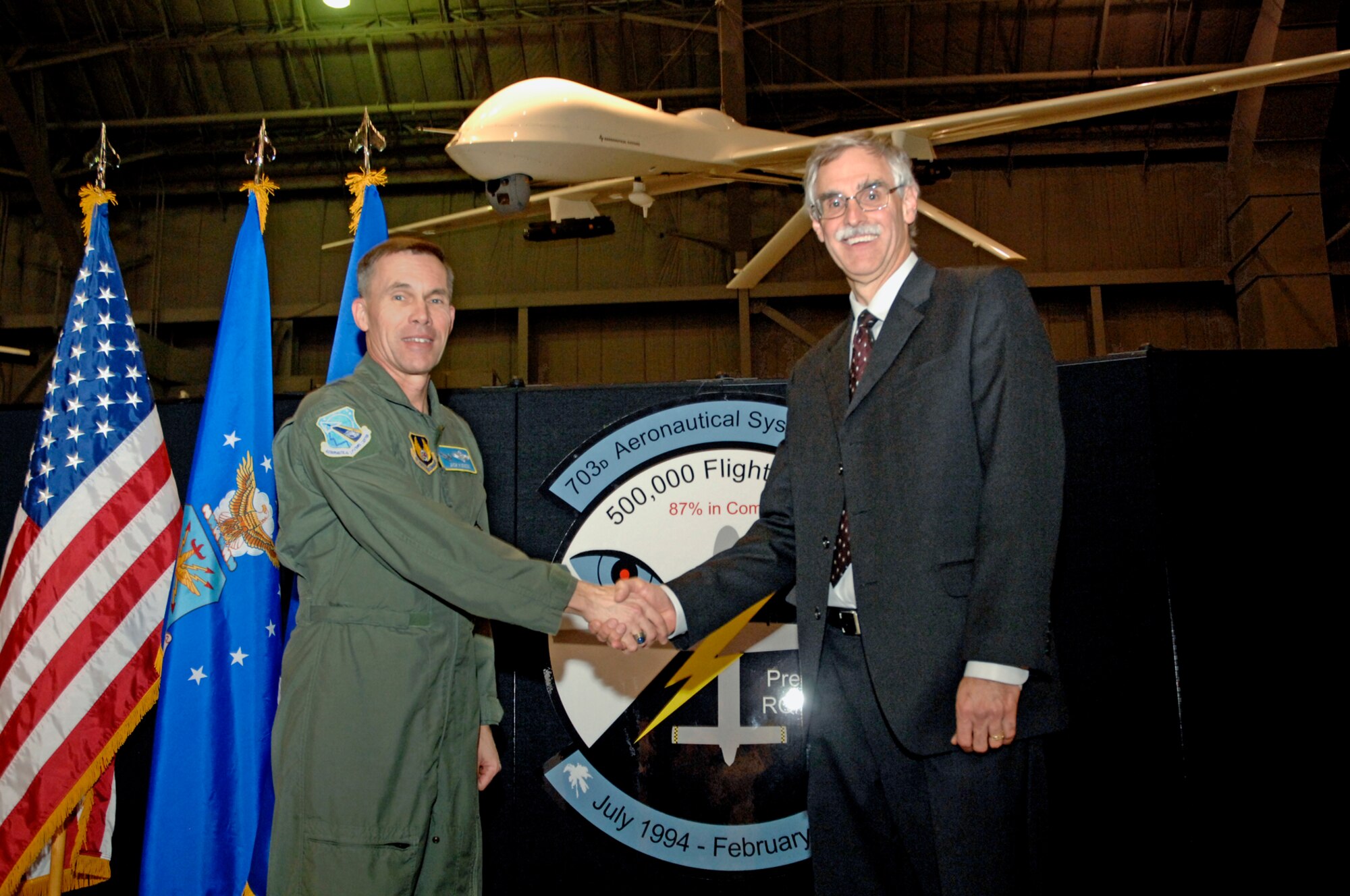 Lt. Gen. Jack Hudson, Aeronautical Systems Center commander at Wright-Patterson Air Force Base, Ohio, and Frank Pace, executive vice president of the aircraft systems group for General Atomics Aircraft Systems, join hands during a Feb. 24 ceremony at the National Museum of the United States Air Force to commemorate more than 500,000 flying hours by the Predator unmanned aircraft system. The milestone was achieved by a Predator flying a combat mission over Iraq on Feb. 18.  Suspended above them is a Hellfire-armed Predator on display in the museum's modern flight gallery. The Predator and Reaper programs are managed by the 703rd Aeronautical Systems Group at Wright-Patt.  (U.S. Air Force photo/Al Bright)