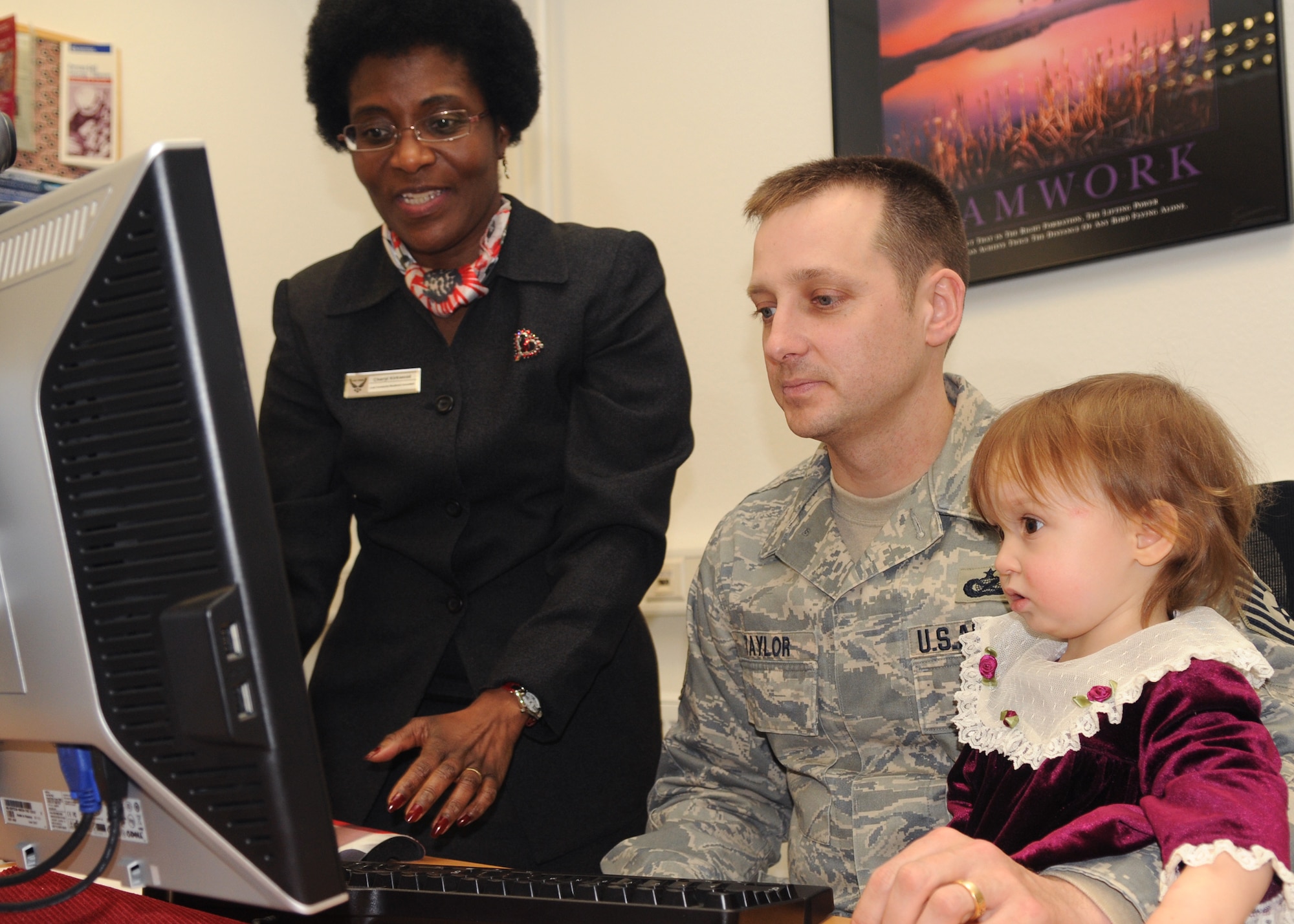 SPANGDAHLEM AIR BASE, Germany – Tech. Sgt. Eugene Taylor, U.S. Air Forces in Europe American Forces Network Detachment 9, holds his daughter, Joy, as Cheryl Kirkwood, Airman & Family Readiness Center, helps him sign up for the Mosel Reintegration Retreat, Feb. 24. The Mosel Reintegration Retreat is a weekend getaway for military couples, offered by the A&FRC. (U.S. Air Force photo by Airman 1st Class Staci Miller)