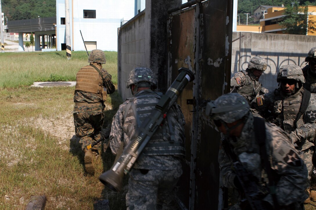 A Marine from 9th Engineer Support Battalion, 3rd Marine Logistics Group, III Marine Expeditionary Force, and soldiers from the U.S. Army's 1st Brigade, Special Troops Battalion, rush a building after clearing their current location during urban breaching and operations training, Sept. 16-19.