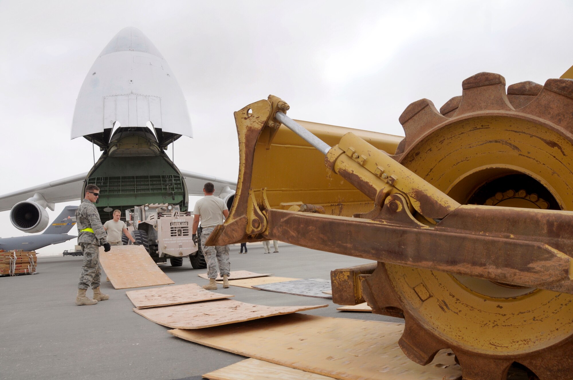 Airman 1st Class Marcus Hines, pavement and construction operator and Airman Brent Koontz, heavy equipment operator both assigned to the 1st Expeditionary Red Horse Group, place one inch thick sheets of plywood in front of a heavy equipment earth compacter to keep it's drive wheels from damaging the flightline pavement Jan. 2, 2009, at an undisclosed air base in Southwest Asia. The earth compacter will be loaded onto a Russian Antonov 124-100 heavy lift cargo aircraft and transported to Afghanistan for work on various Red Horse concrete projects.  Airman Hines, a native of Durant Okla., is deployed from Altus AFB, Okla., Airman Koontz, a native of Hagerstown, Md., is deployed from Nellis Air Force Base, Nev., both are deployed in support of Operations Iraqi and Enduring Freedom and Joint Task Force-Horn of Africa. (U.S. Air Force photo by Staff Sgt. Darnell T. Cannady/Released)