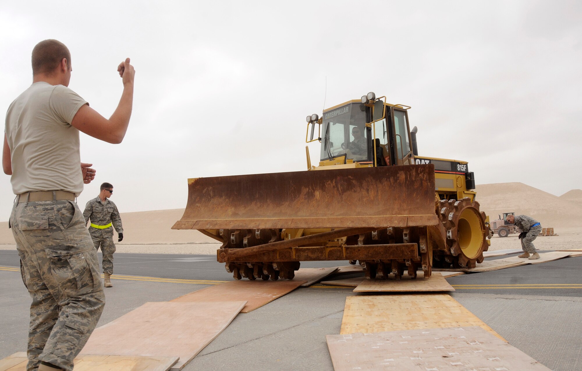 Airman Brent Koontz, heavy equipment operator, Airman 1st Class Marcus Hines, pavement and construction operator, and Master Sgt. Jon Hopp, non commissioned officer in charge of airfields, all assigned to the 1st Expeditionary Red Horse Group, guide a heavy equipment earth compacter onto one inch thick sheets of plywood to keep it's drive wheels from damaging the flightline pavement Jan. 2, 2009, at an undisclosed air base in Southwest Asia. The earth compacter will be loaded onto a Russian Antonov 124-100 heavy lift cargo aircraft and transported to Afghanistan for work on various Red Horse concrete projects. Airman Koontz, a native of Hagerstown, Md., is deployed from Nellis Air Force Base, Nev., Airman Hines, a native of Durant Okla., is deployed from Altus AFB, Okla., and Sergeant Hopp, a native of Milwaukee, Wis., is also deployed from Nellis AFB, Nev.  All are deployed in support of Operations Iraqi and Enduring Freedom and Joint Task Force-Horn of Africa. (U.S. Air Force photo by Staff Sgt. Darnell T. Cannady/Released)