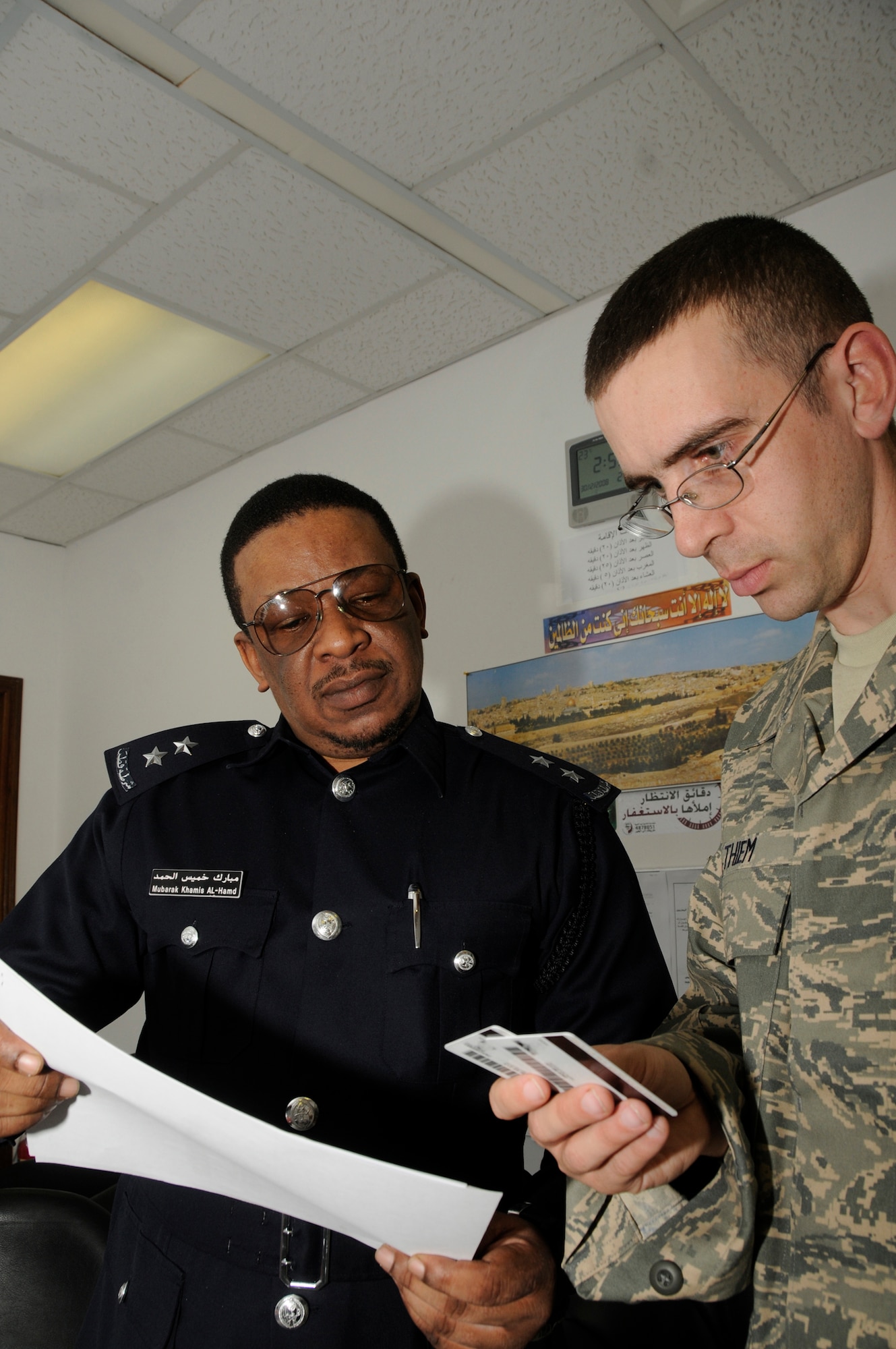 Staff Sgt. Norman Thiem, immigration liaison assigned to the 379th Air expeditionary Wing, checks indentification cards against information on an in processing worksheet with local national immigration personnel. The immigration liaison is responsible for ensuring all members can deploy into and out of deployed locations and that all personnel respect the host nation's laws. Sergeant Thiem, a native of Tuscumbia, Ala., is deployed from Travis Air Force Base, Calif. (U.S. Air Force photo by Staff Sgt. Darnell T. Cannady)